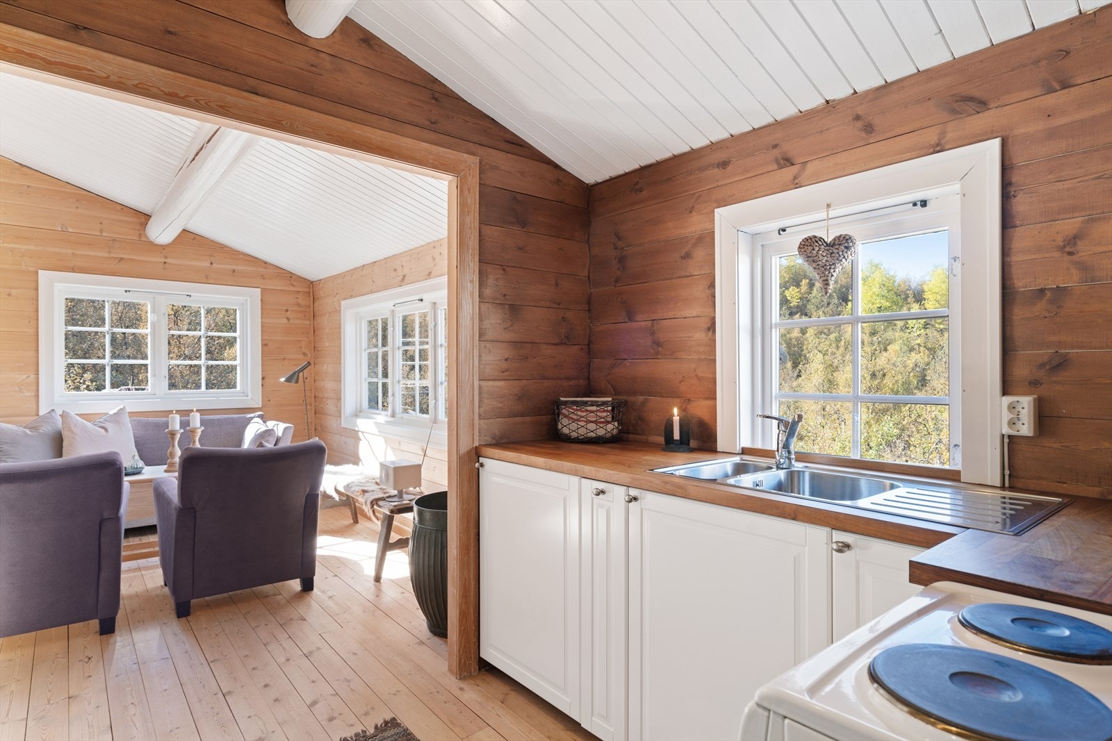 Lysmalt kjøkkeninnredning med benkeskap, og vaskekum i laminat benkeplate, samt frittstående komfyr og integrert kjøleskap. Galleribilde