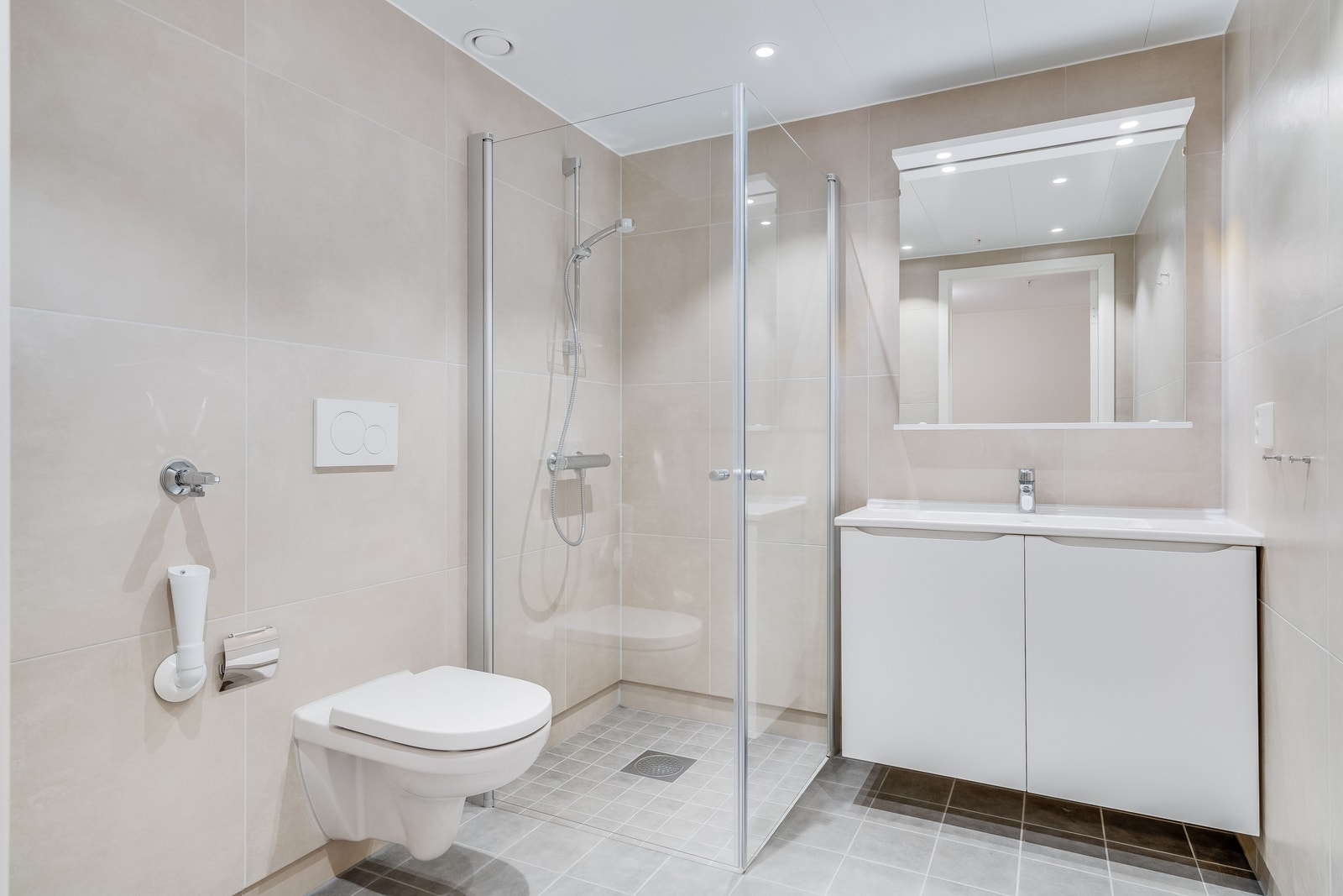 Flott, flislagt bad med veggehengt toalett, opplegg for vaskemaskin og spotbelysning i tak Galleribilde