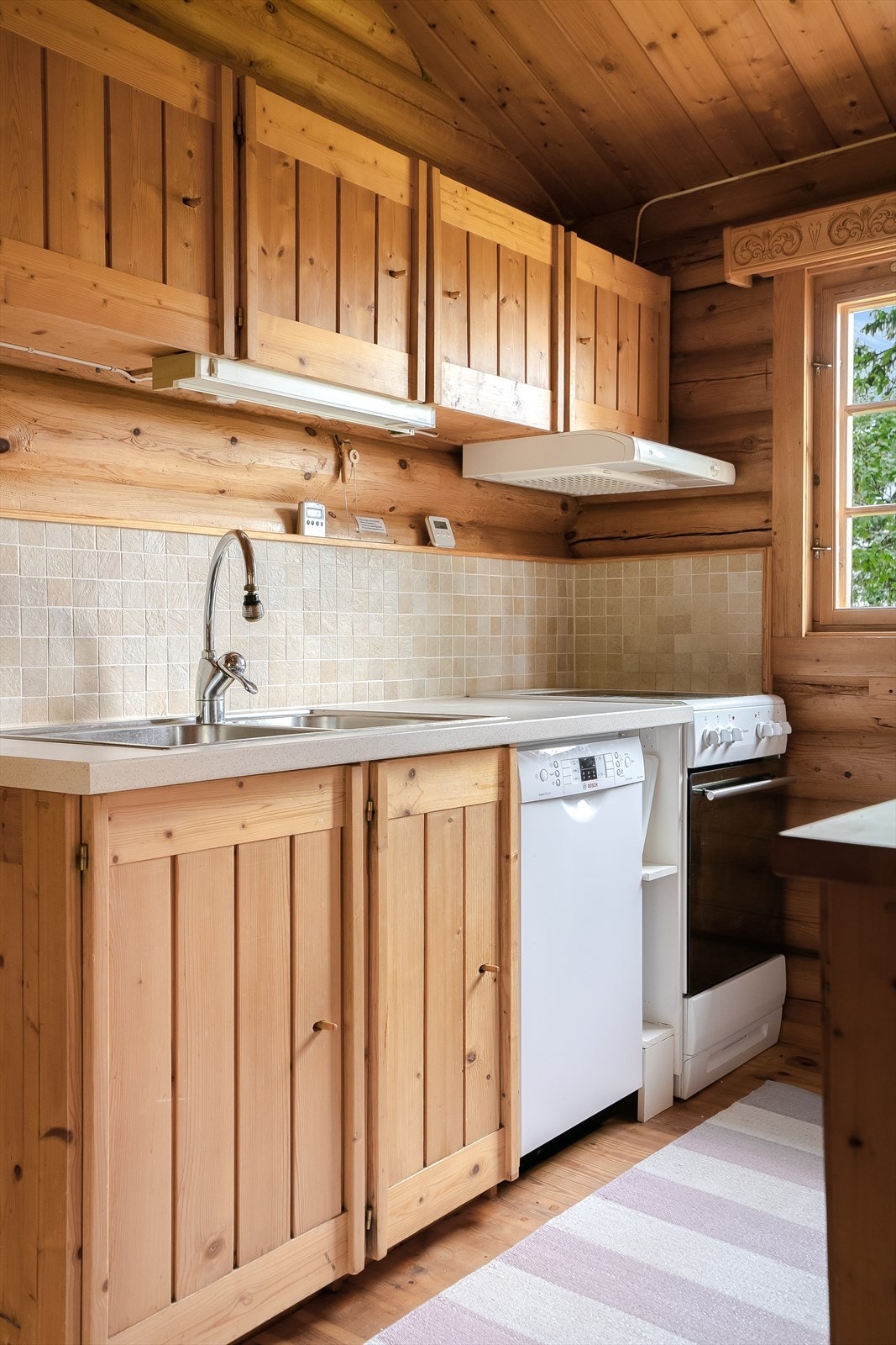 Stålkum med ett-greps blandebatteri, kjøkkenvifte over komfyr og lys under overskap Galleribilde