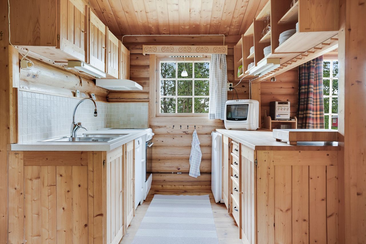 Originalt kjøkken med profilerte heltre fronter, fliser på vegg mellom over- og underskap og nyere benkeplate ved vaskesone. Åpen løsning for oppvaskmaskin, komfyr og kjøleskap Galleribilde