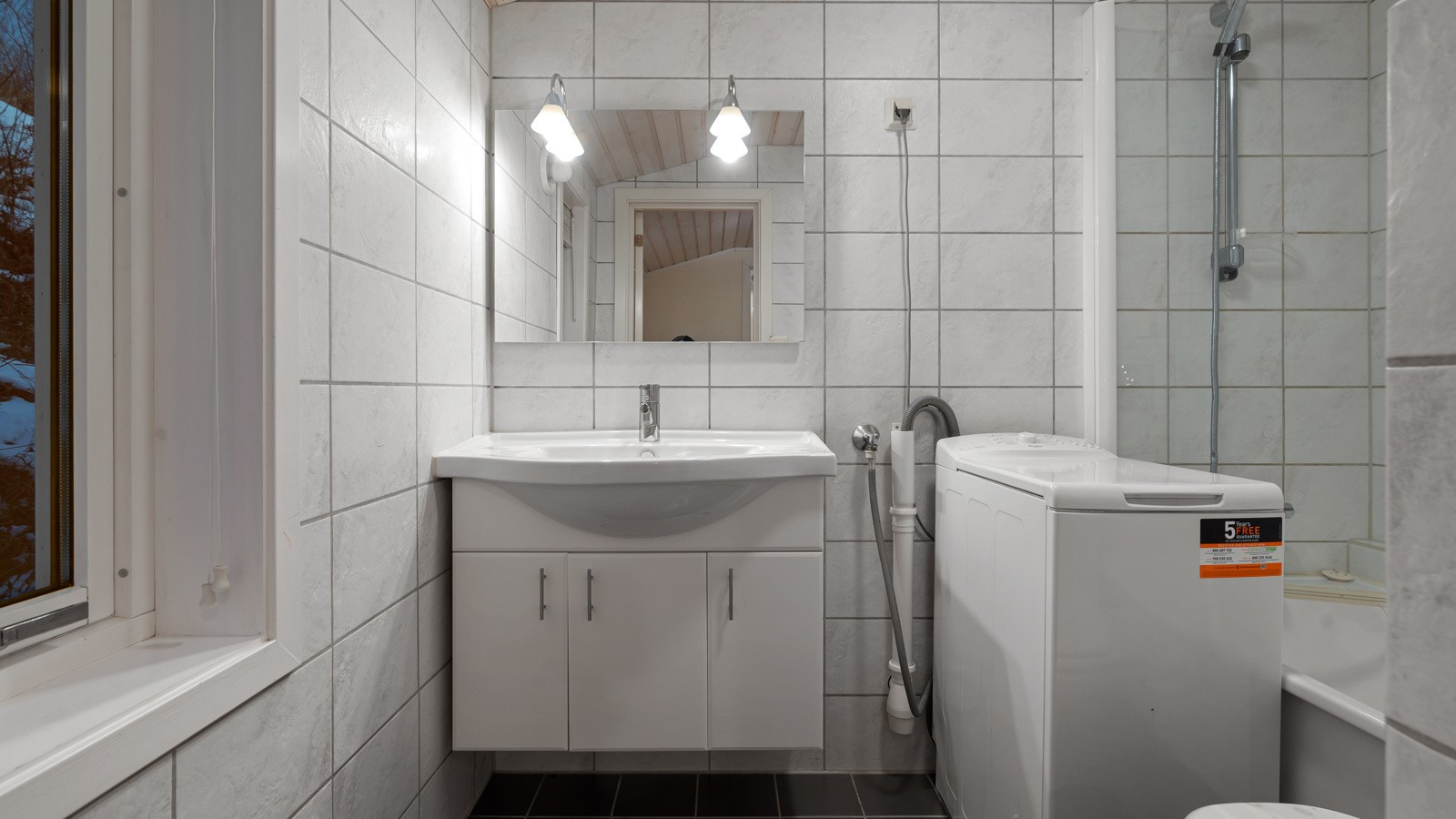 Bad med servantskap, badekar, toalett og opplegg for vaskemaskin.
