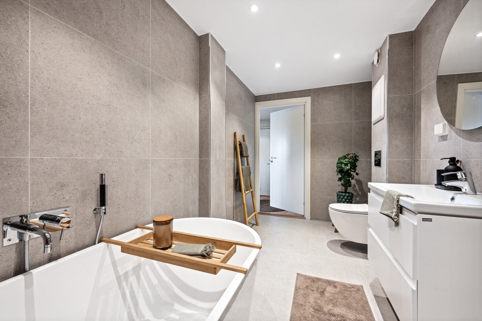 Badet er innredet med vegghengttoalett, servant med underskap, speil med belysning, dusjhjørnet i herdet glass, badekar og opplegg for vaskemaskin. Det er varmekabler i gulvet. Galleribilde