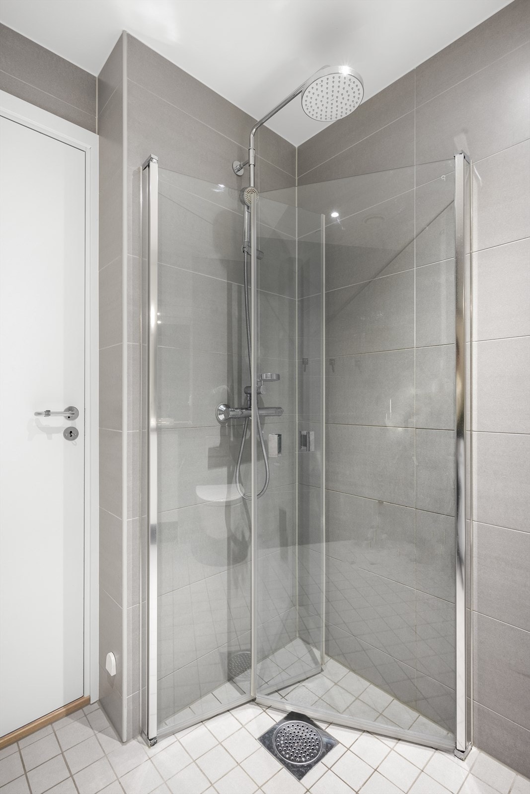 Baderomsinnredningen består av servant i benkeskap, veggmontert wc og dusjhjørne med innfellbare glassdører. Galleribilde