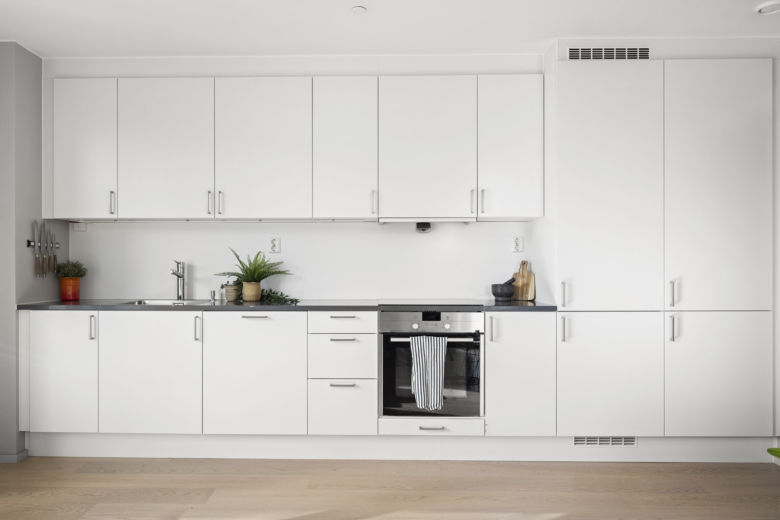 Hvit, glatt kjøkkeninnredning med steinbenkt benkeplate og nedfelt oppvaskkum. Galleribilde