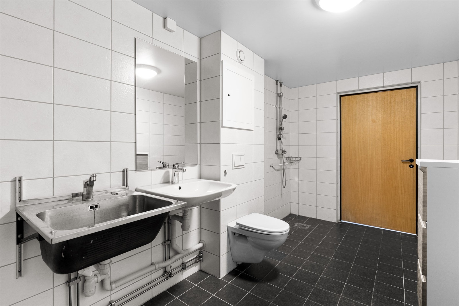 Flislagt bad/wc med dusj, vegghengt toalett, utslagsvask og speil over servant Galleribilde