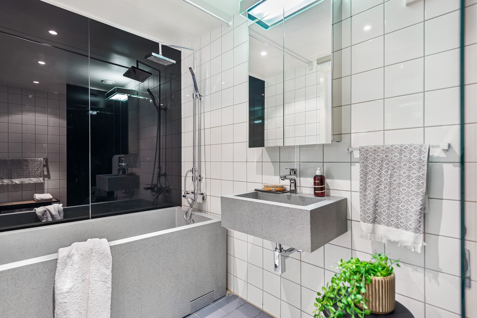 Badet er innredet med vegghengt servant, speilskap med belysning over servant, frittstående badekar med regn- og hånddusj og opplegg for vaskemaskin. Galleribilde