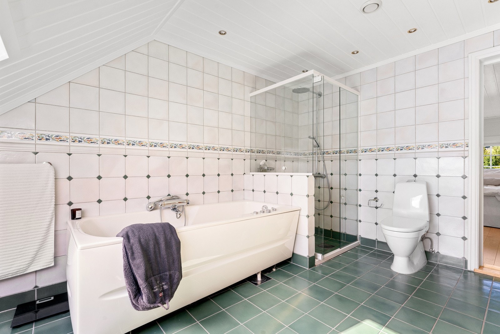 Videre er badet innredet med to nedfelte servanter, gulvstående toalett, frittstående boblebadekar og dusjhjørne med hånddusj og regnfallsdusj. Galleribilde