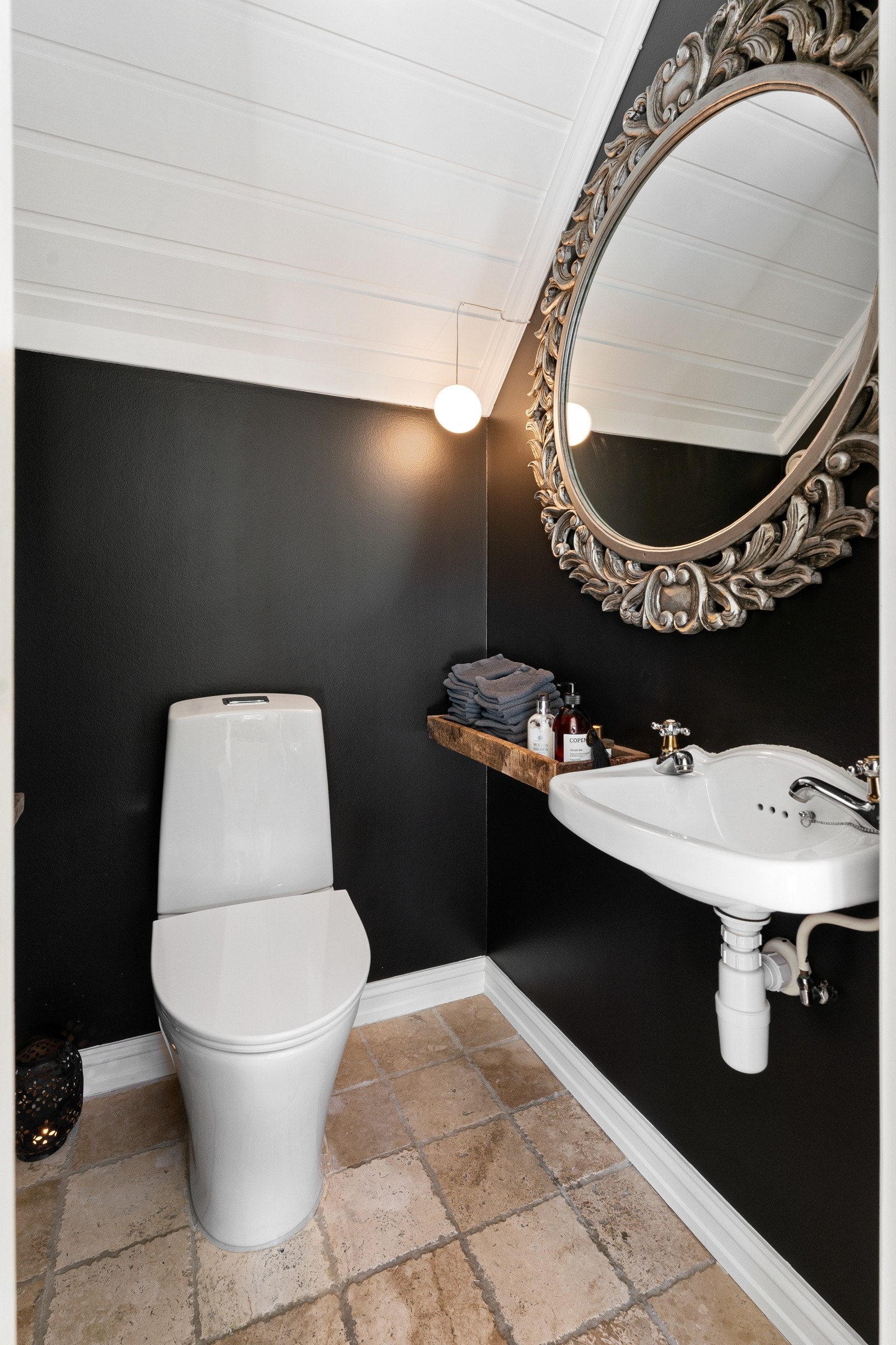 Toalettrommet ligger i forbindelse med entreen. Rommet er innredet med gulvstående toalett og servant i nostalgisk stil. Det er beige marmorfliser i rustikk stil og gulvvarme. Galleribilde