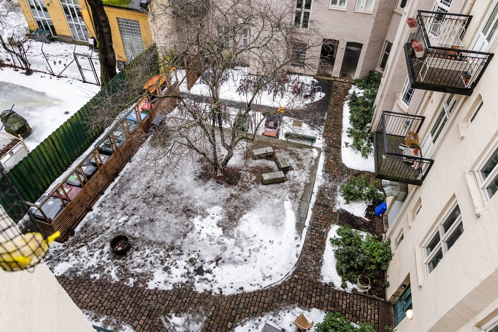 Utsyn ned til den flotte bakgården med sittegrupper, stensatte gangveier, beplantning og sykkelparkering Galleribilde