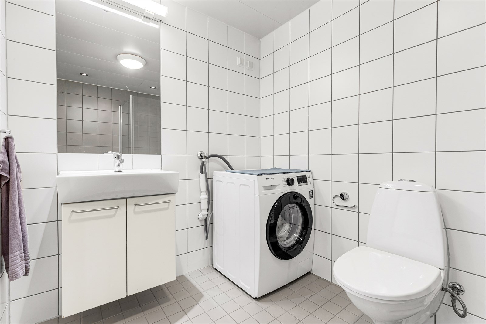 Flislagt baderom fra 2005 med underskap, heldekkende servant og veggmontert overskap med speil og lampe. Det er opplegg for vaskemaskin. Galleribilde