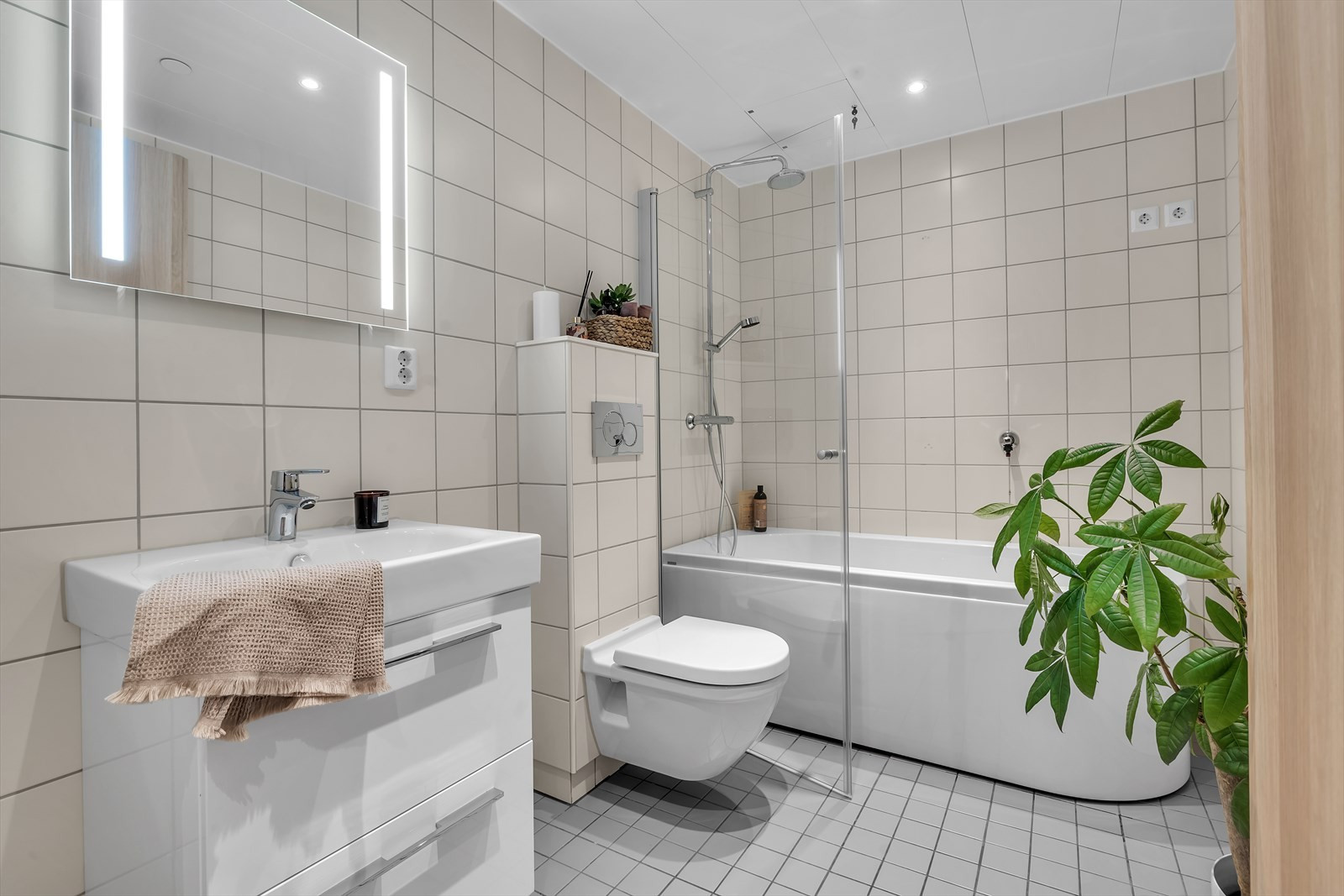 Lyst og moderne bad med badekar, vegghengt WC, speil med lys