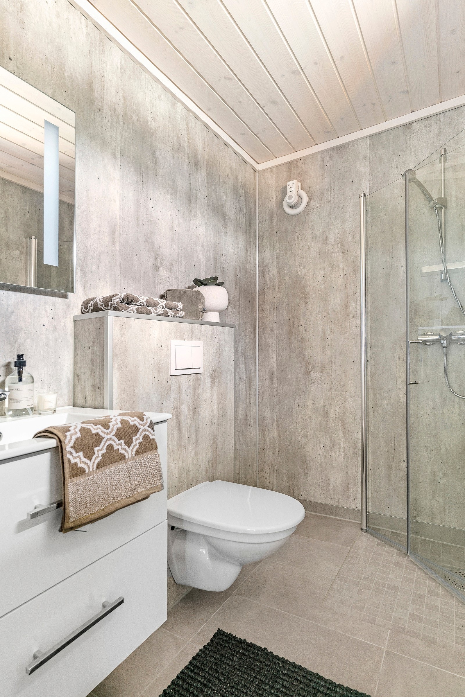 Lekkert baderom med gulvfliser, våtromsplater på vegg, dusjhjørne, vask i skuffeseksjon med speil og vegghengt toalett Galleribilde