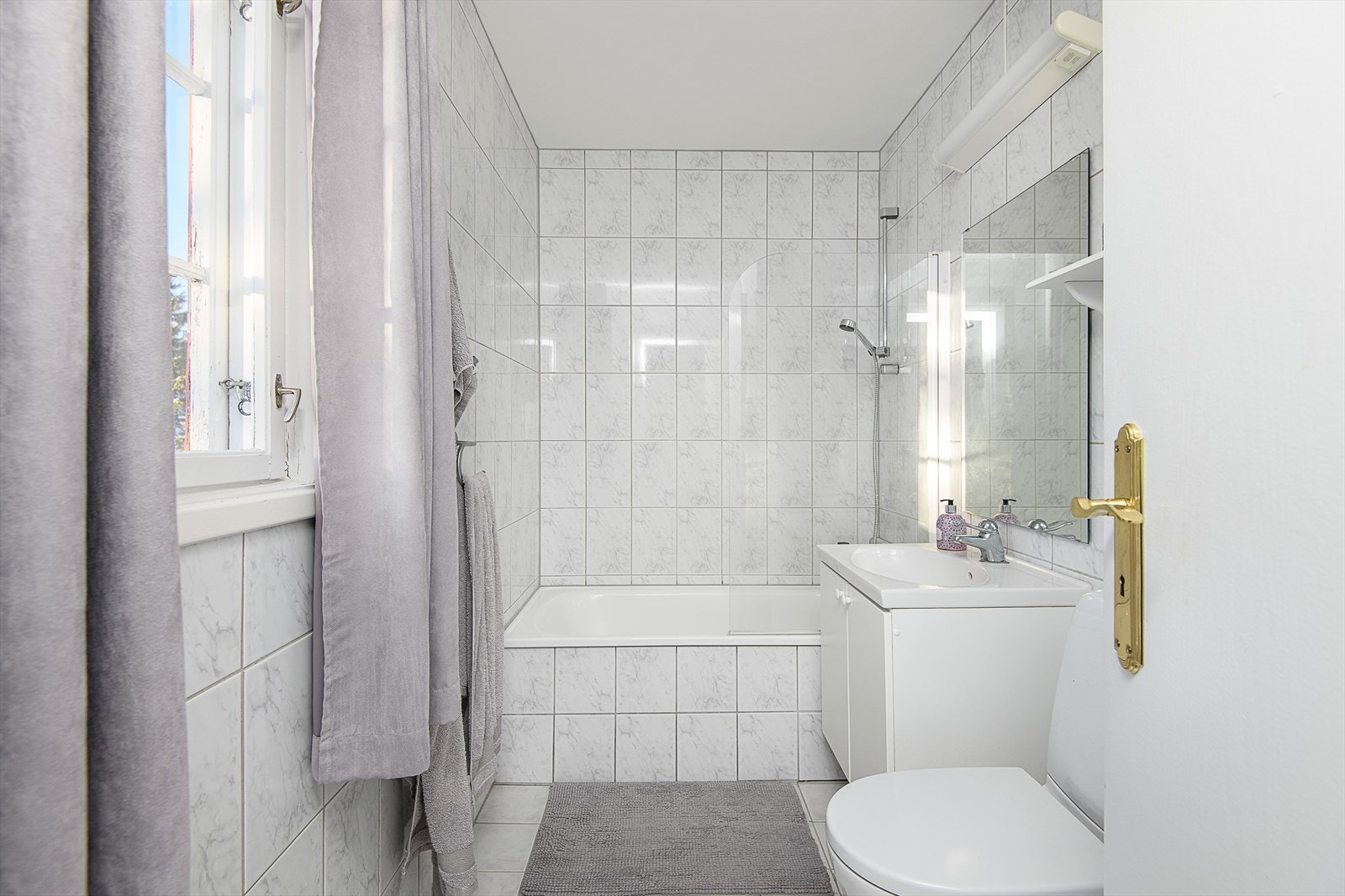 Badets overflater består av fliser. Innredet med servant med underskap, speil med tilhørende belysning, badekar og gulvmontert WC. Komfortabel varme i gulv. Galleribilde