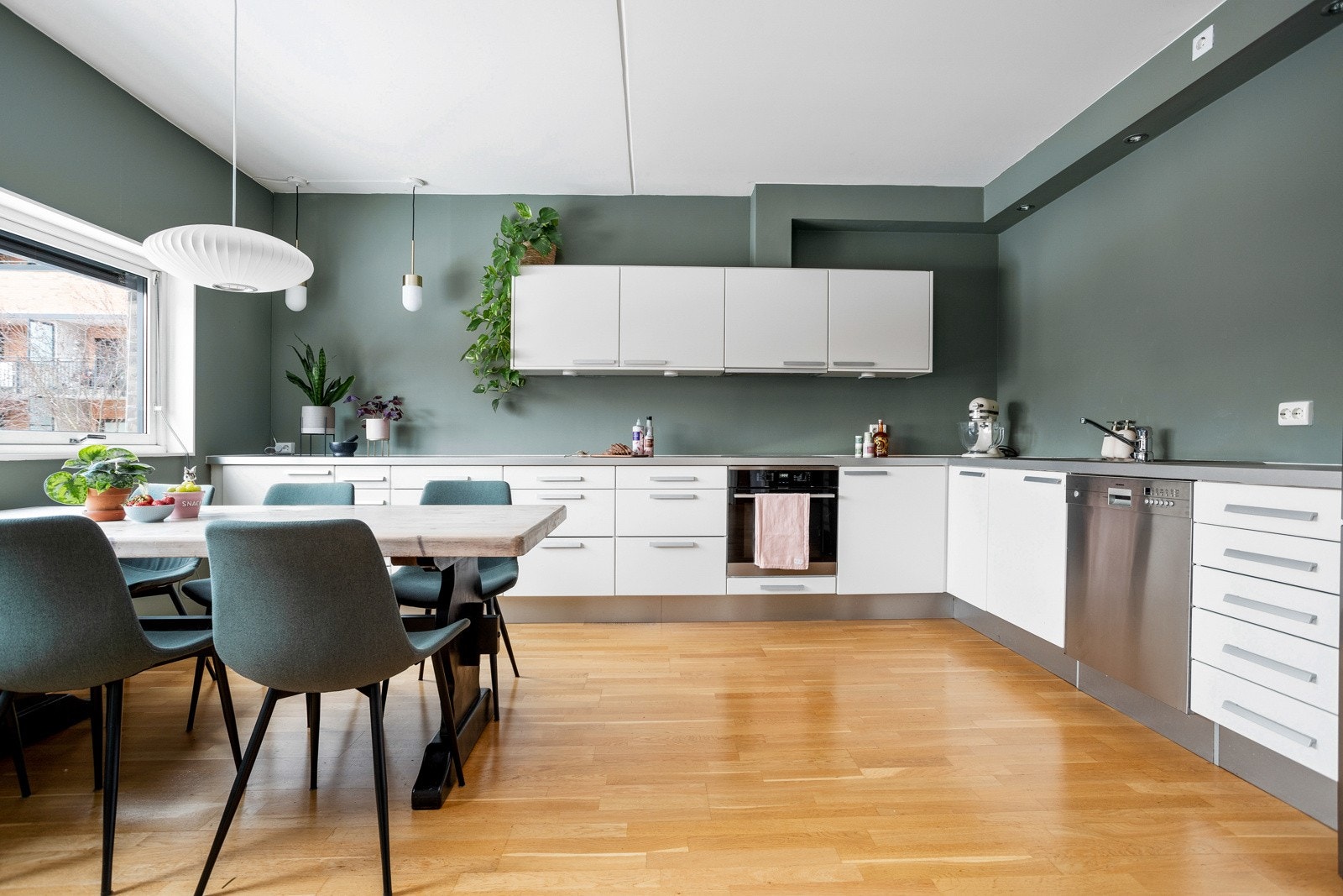 Tidløs kjøkkeninnredning fra Sigdal med slette fronter og stålhåndtak, samt overskap med benkebelysning over deler av benkeplaten. Lys laminat benkeplate med nedfelt stålkum og ett-greps armatur i krom. Galleribilde