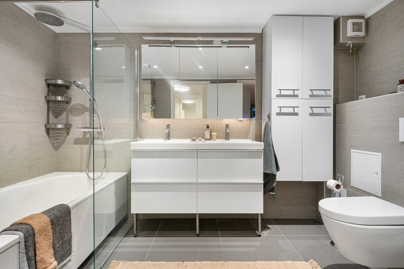 Badet er utstyrt med badekar med dusj, dobbeltservant med skuffer og speilskap, høyskap og vegghengt toalett.Det er enkelt å fjerne badekaret om man ønsker en enda større dusjsone Galleribilde