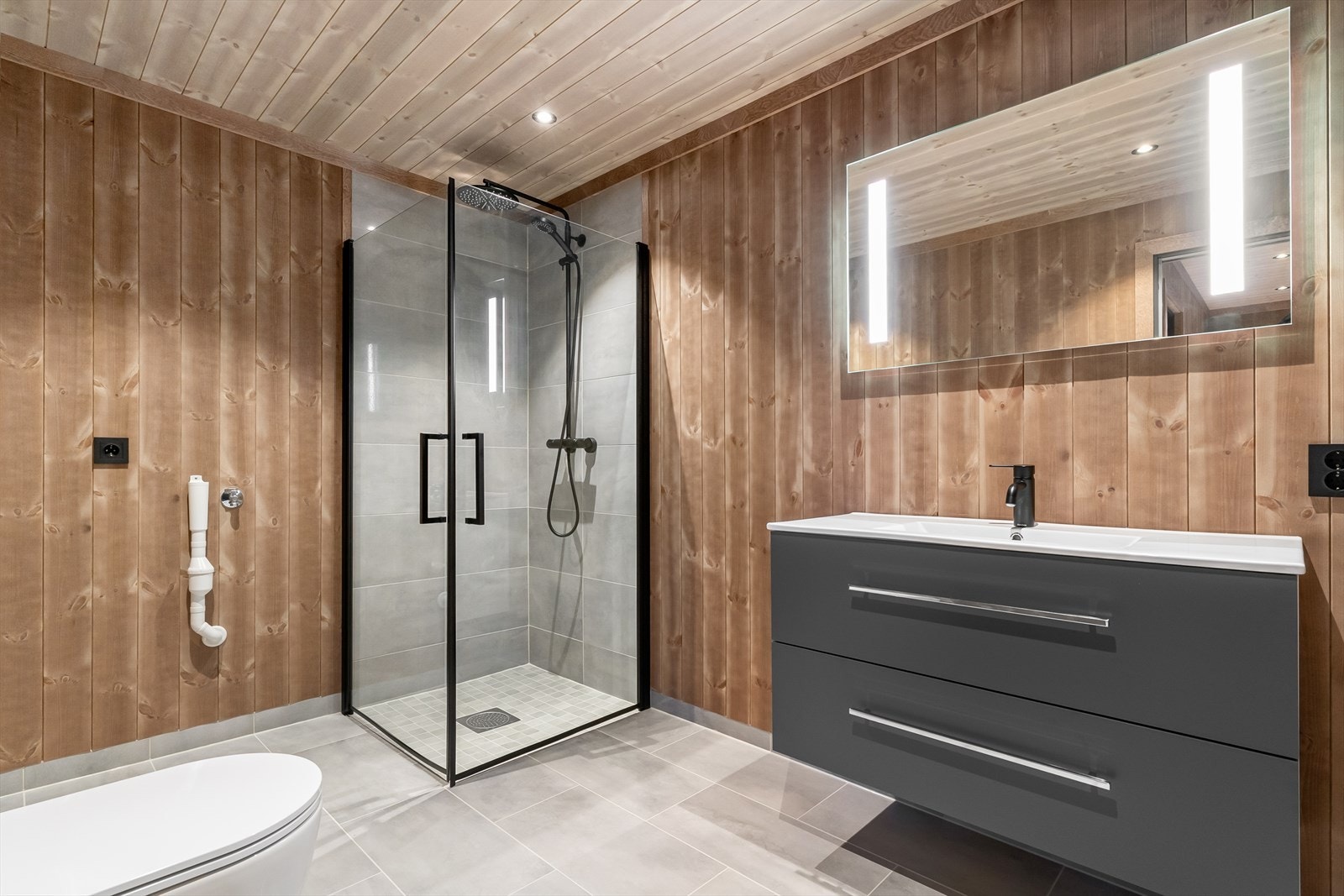 Bad i utleiedel/ gjesteleilighet med sanitærutstyr bestående av baderomsinnredning med speil over, dusjhjørne med fliser på vegg - glass dusjvegger og vegghengt toalett Galleribilde