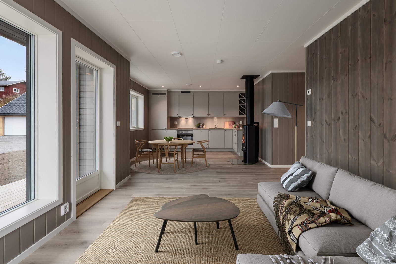 Åpen stue og kjøkken-løsning med store vinduer og mange mulighet for møblering. Lune og moderne farger. Digitalt møblert. Galleribilde