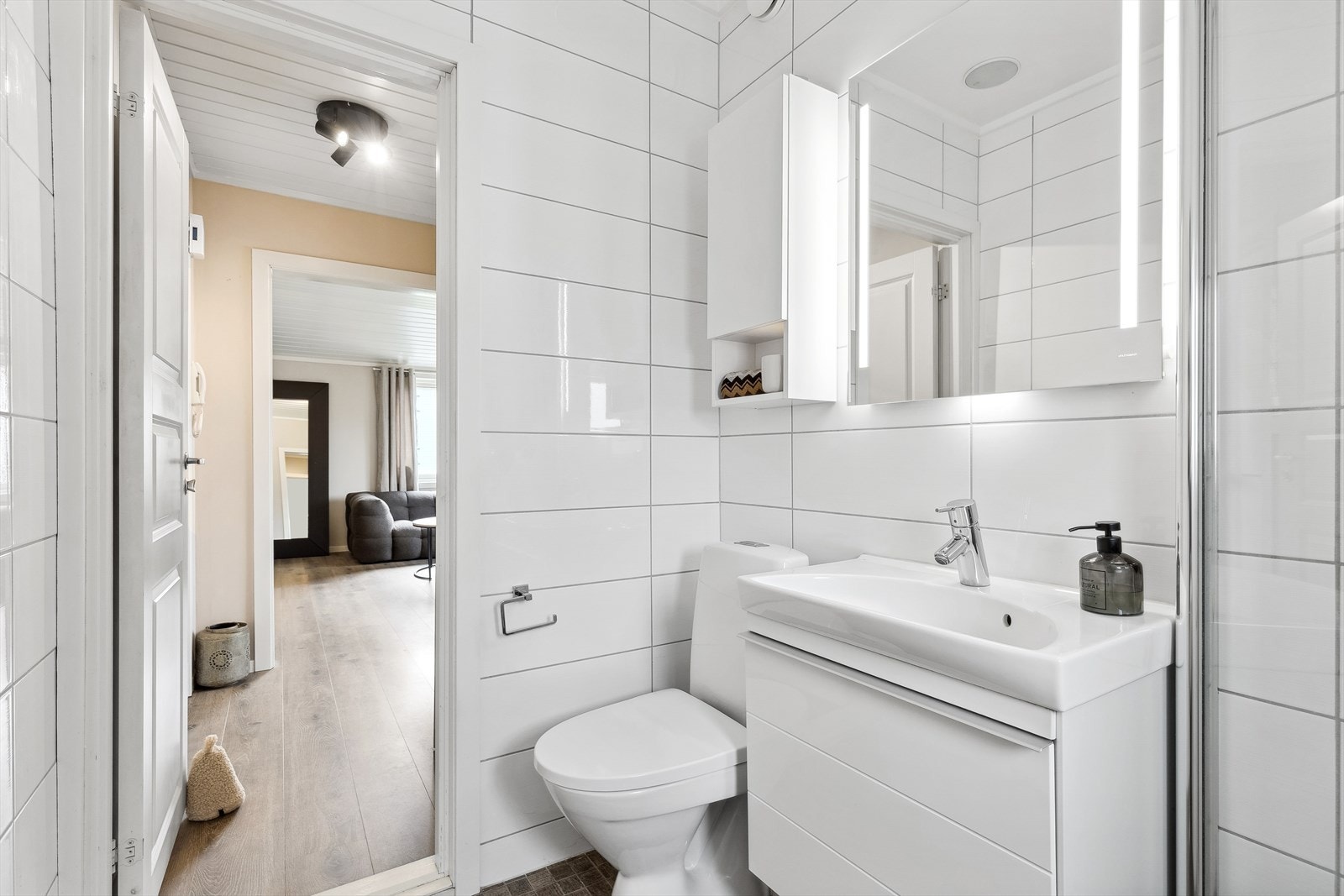 Badet er innredet med toalett, dusjhjørne med vegg/dør i herdet glass, servantinnredning, overskap og speil med belysning. Galleribilde