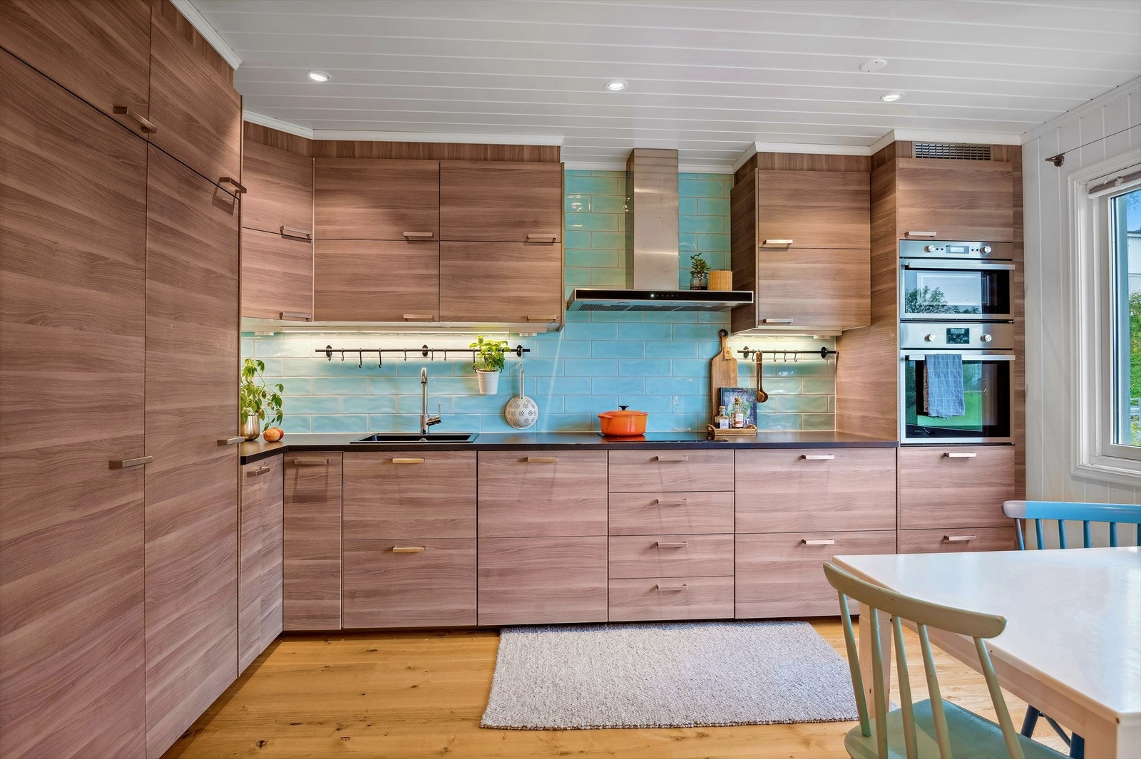Moderne innredning fra ca. 2015 med slette folierte fronter i treimitasjon, laminert benkeplate m/kjøkkenkum og fliser på vegg over benk Galleribilde