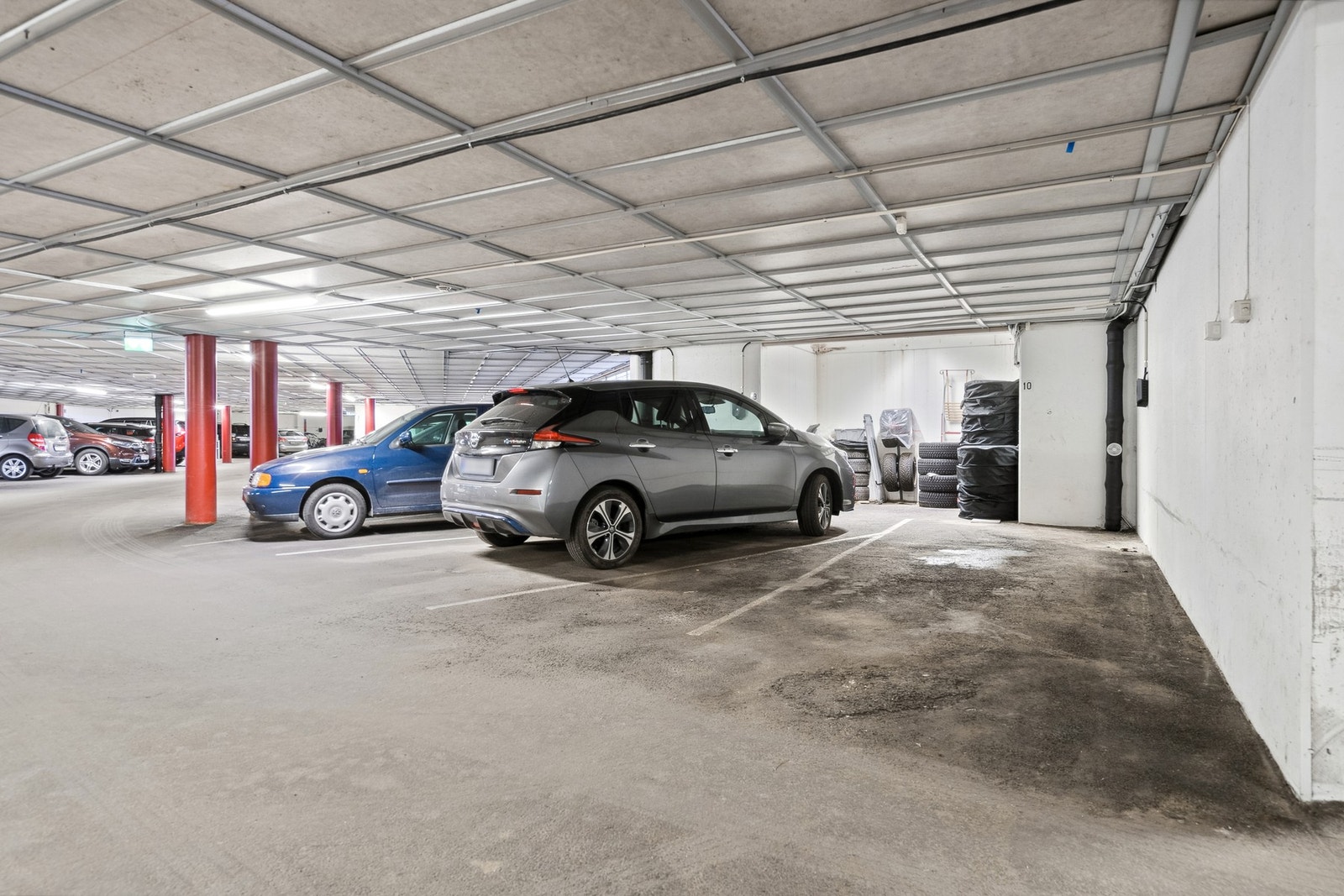 Romslig oppmerket parkeringsplass i kjeller med mulighet for el-bil lader. Galleribilde