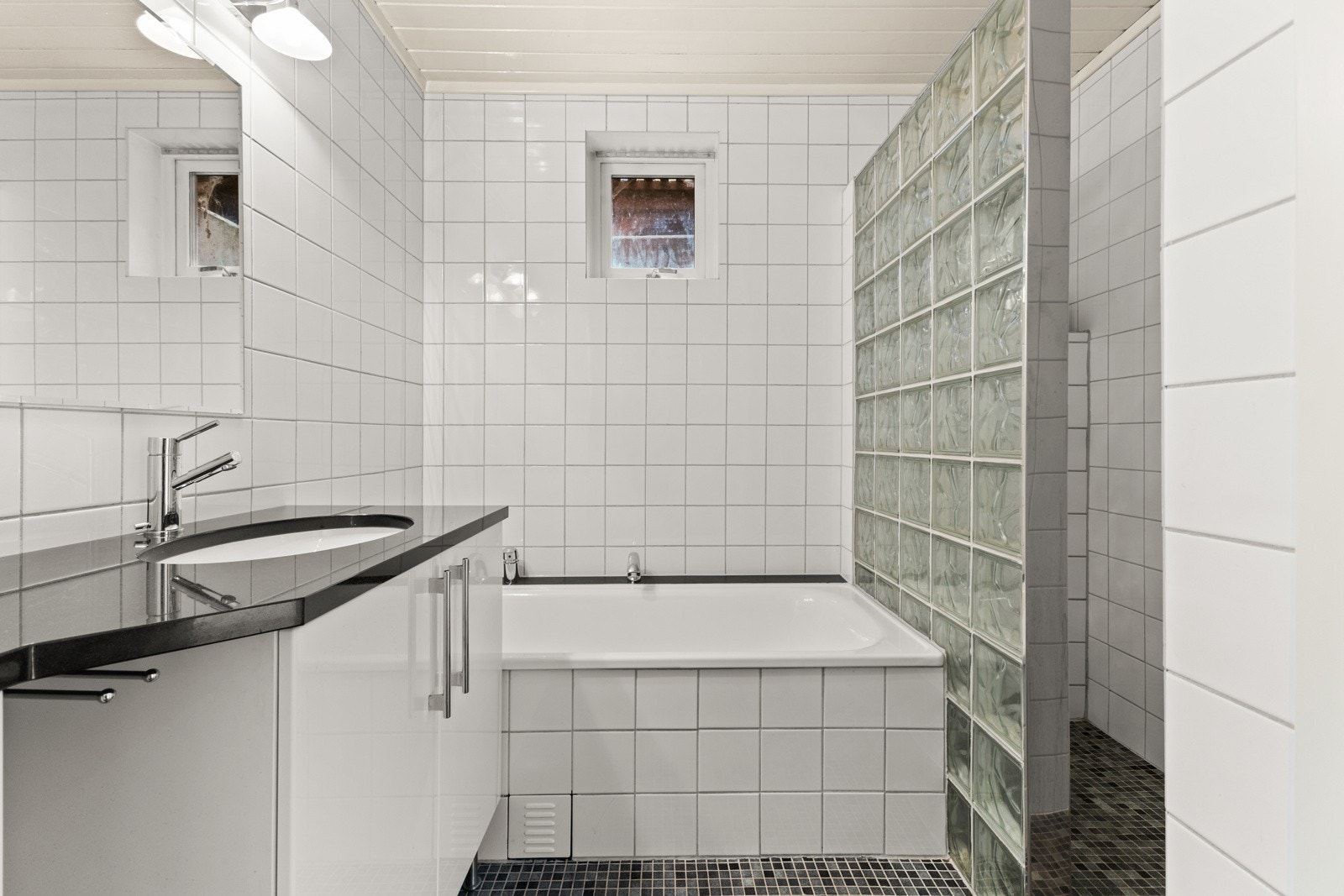 Flislagt pent bad med varmekabler, innmurt badekar og dusjhjørne med skillevegg i glassbyggerstein. Galleribilde