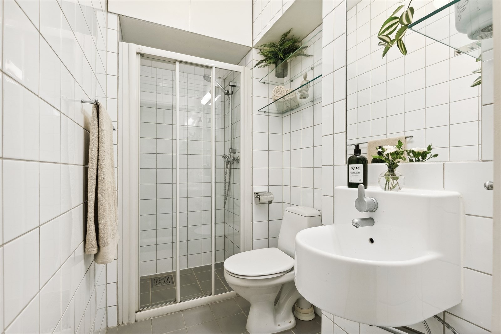 Baderommet inneholder dusjnisje med justerbart dusjhode og skyvedør i herdet glass. Servant og gulvstående klosett. Glasshyller for oppbevaring av håndklær/toalettsaker. Varmekabler i gulv. Galleribilde