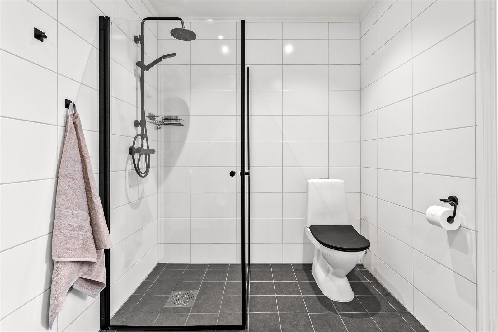 Innredningen består av gulvmontert wc, dusjsone med fossefalldusj og dusjvegger med svarte detaljer, samt servant i skuffeseksjon med speilskap og belysning over. Galleribilde