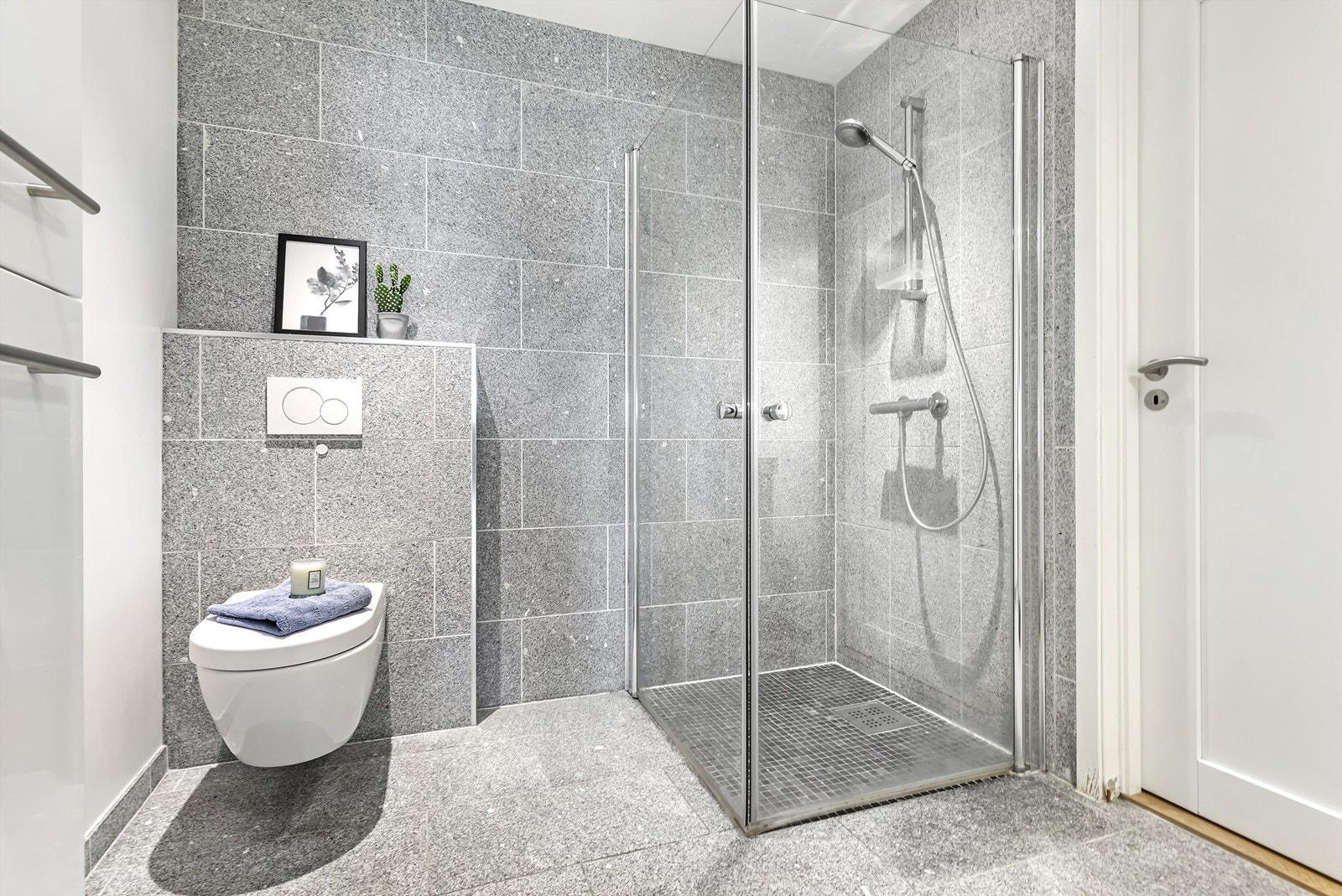 Pent bad utstyrt med servantskap med heldekkende servant, veggmontert WC og dusj med glassdører. Galleribilde