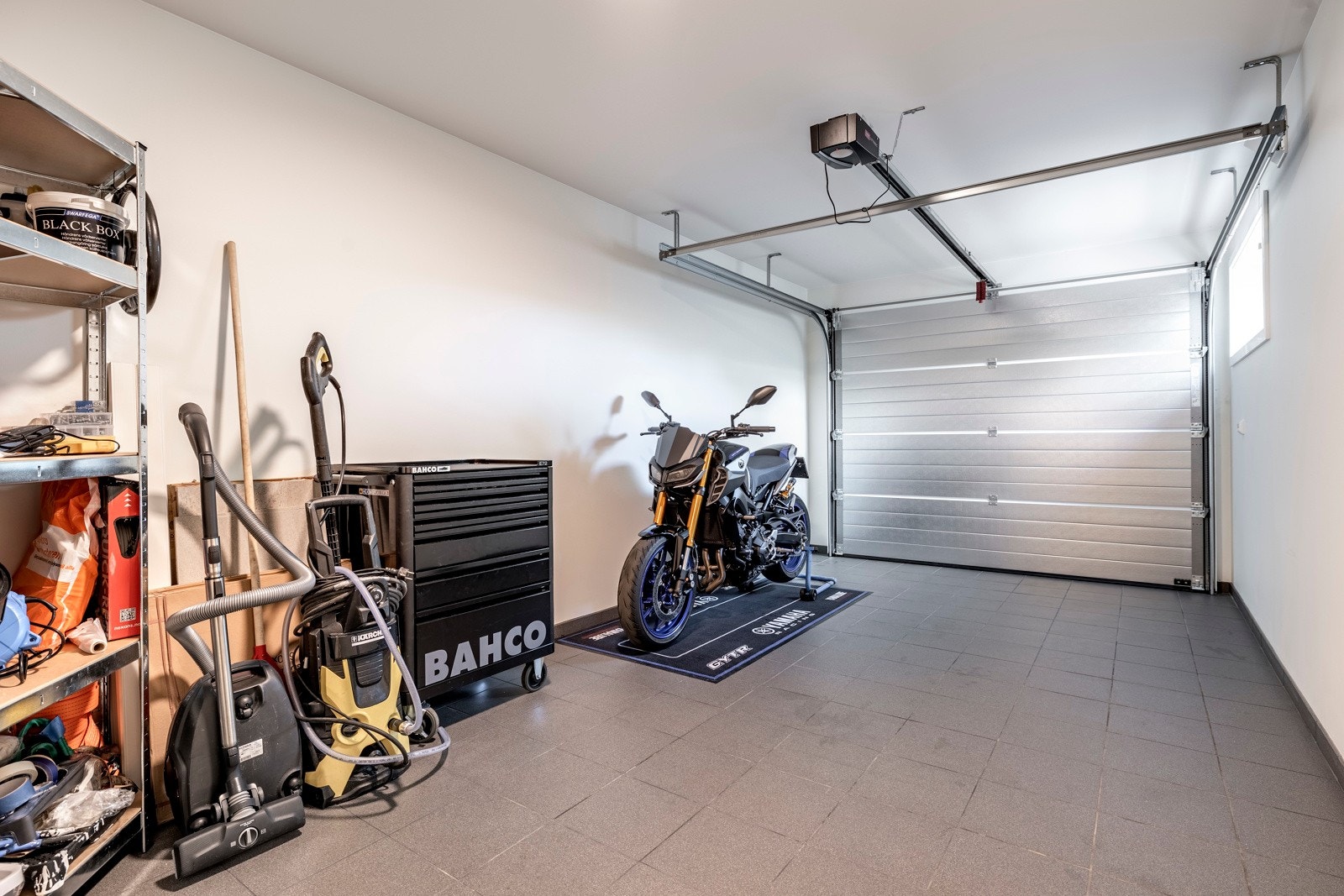 Det er parkering i en integrert garasje med motorisert portåpner, og her kan man gå tørrskodd inn i huset i all slags vær. Galleribilde