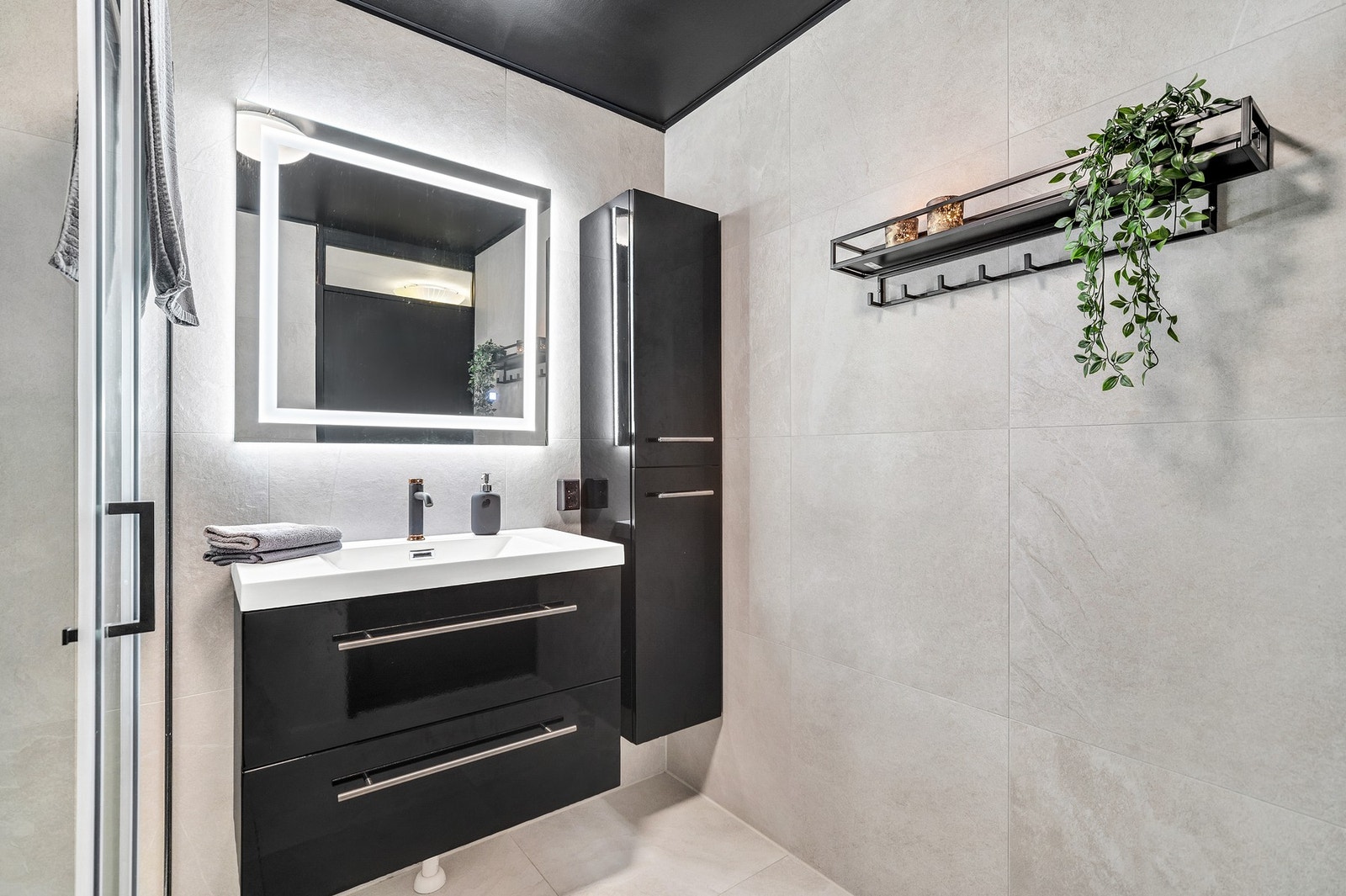 Sorte detaljer er en gjenganger på badet og komplimenterer de beige 60x60-flisene svært godt. God oppbevaringsplass i baderomsinnredningen. Galleribilde