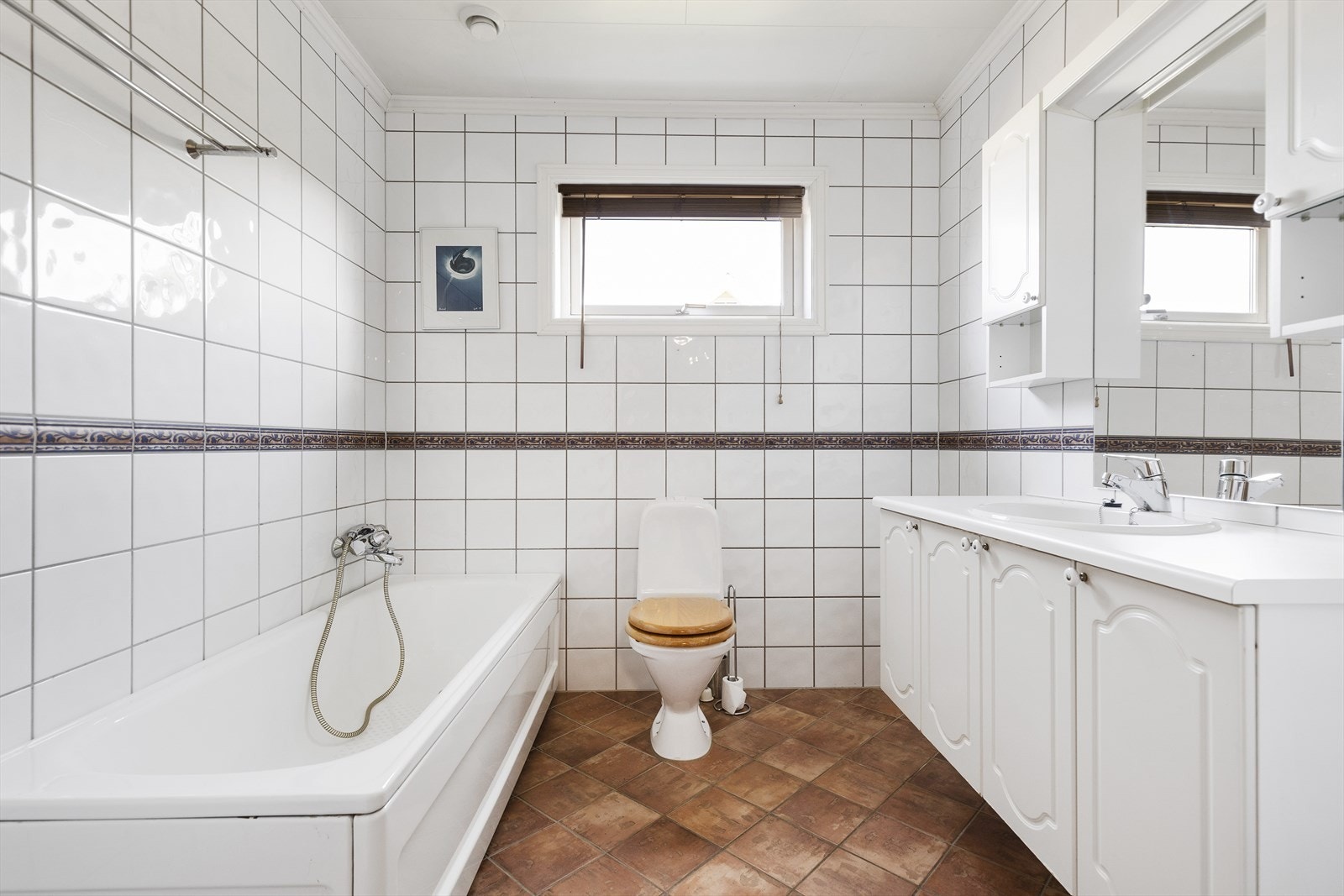 Flislagt bad med keramiske fliser. Badet er utstyrt med frittstående toalett, badekar med dusj og servantinnredning med skap og speil. Galleribilde
