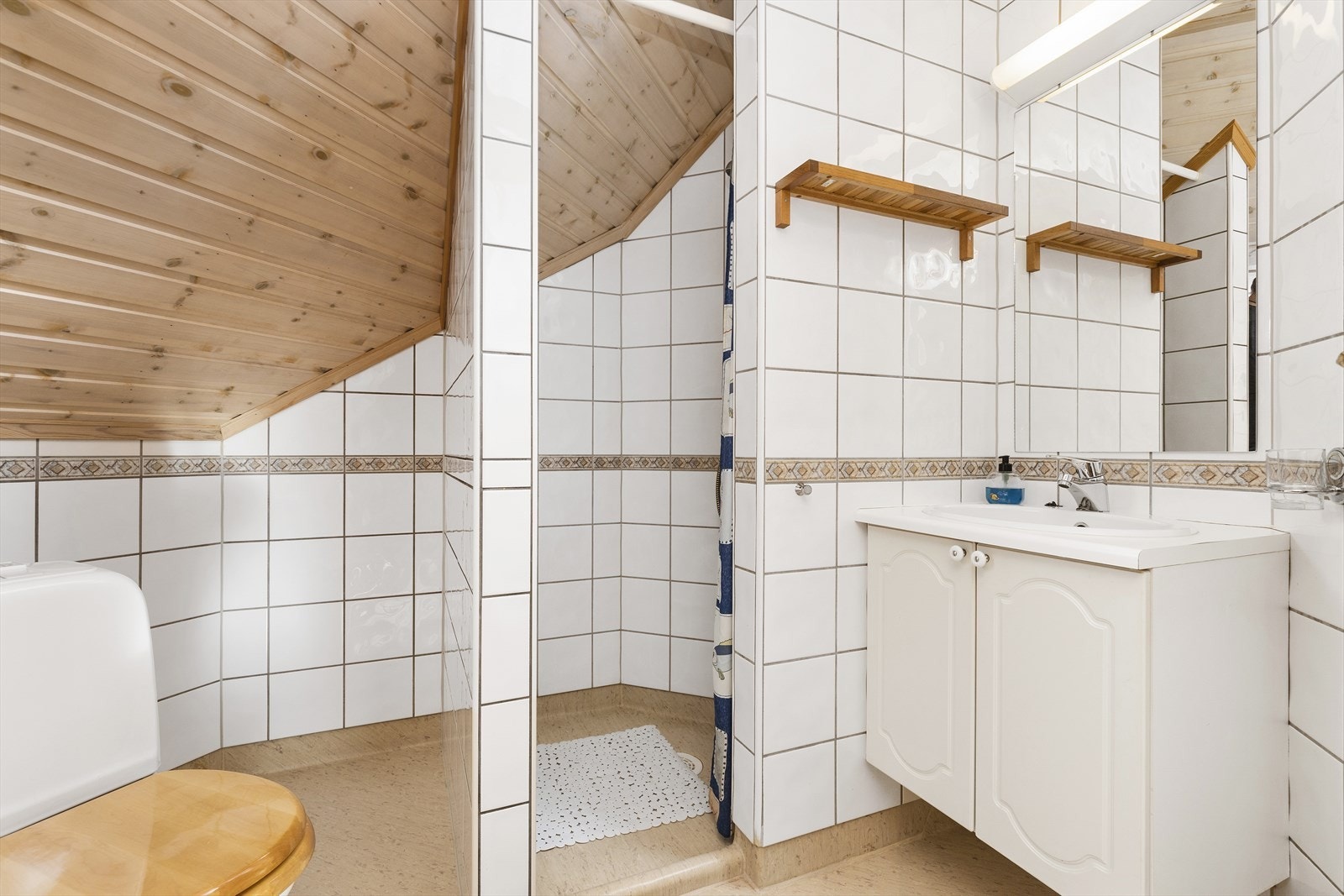 Badet har flislagte vegger og gulv/sokkel med belegg. Det er laget internt fall i dusjnisje med sokkelkant mot åpning. Frittstående toalett og servantinnredning. Galleribilde