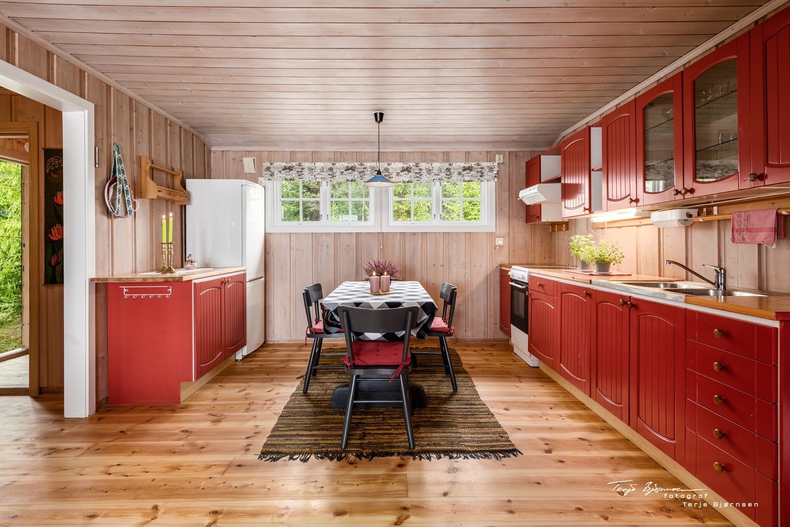 Kjøkkenet er innredet med under- og overskap, malte profilerte dører/ fronter (heltre) i en behagelig rødfarge som gir en fin kontrast til trepanelen. Galleribilde