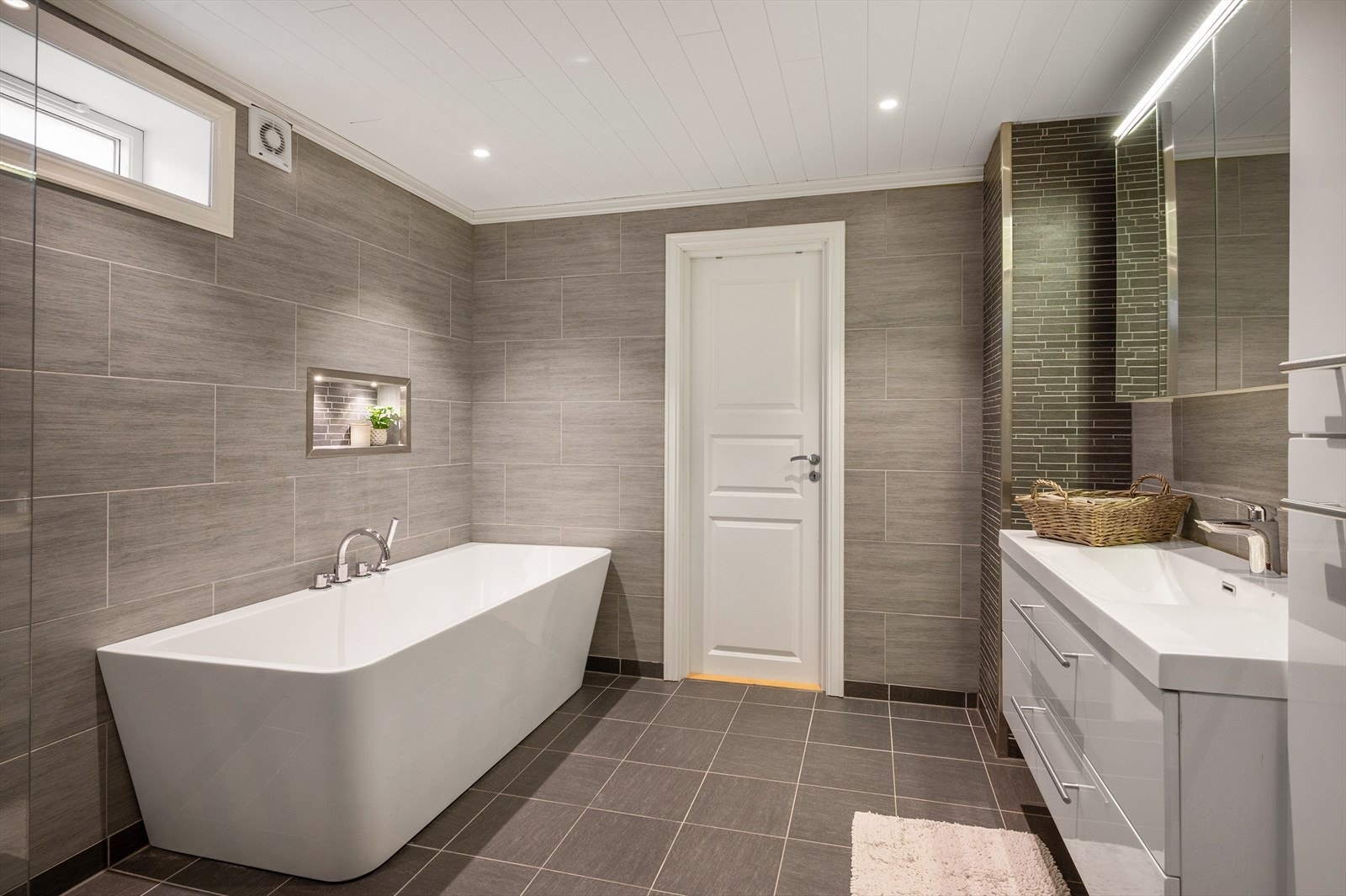 Romslig og pent bad som er utført i samme stil som badet i 1. etasje. Dette er også fra 2015. På overflater er det flislagte gulv med elektriske varmekabler, flislagte vegger og malt panel i himling. Galleribilde