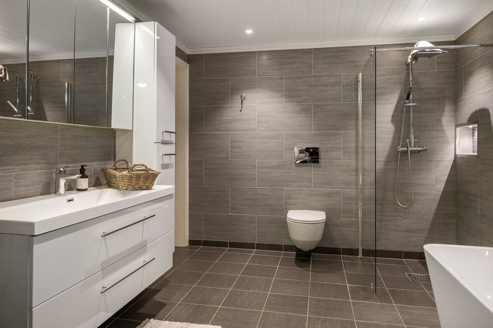 Badet har baderomsinnredning med heldekkende servant og overskap med speildører, høyskap, badekar, dusjvegger og vegghengt toalett. Galleribilde