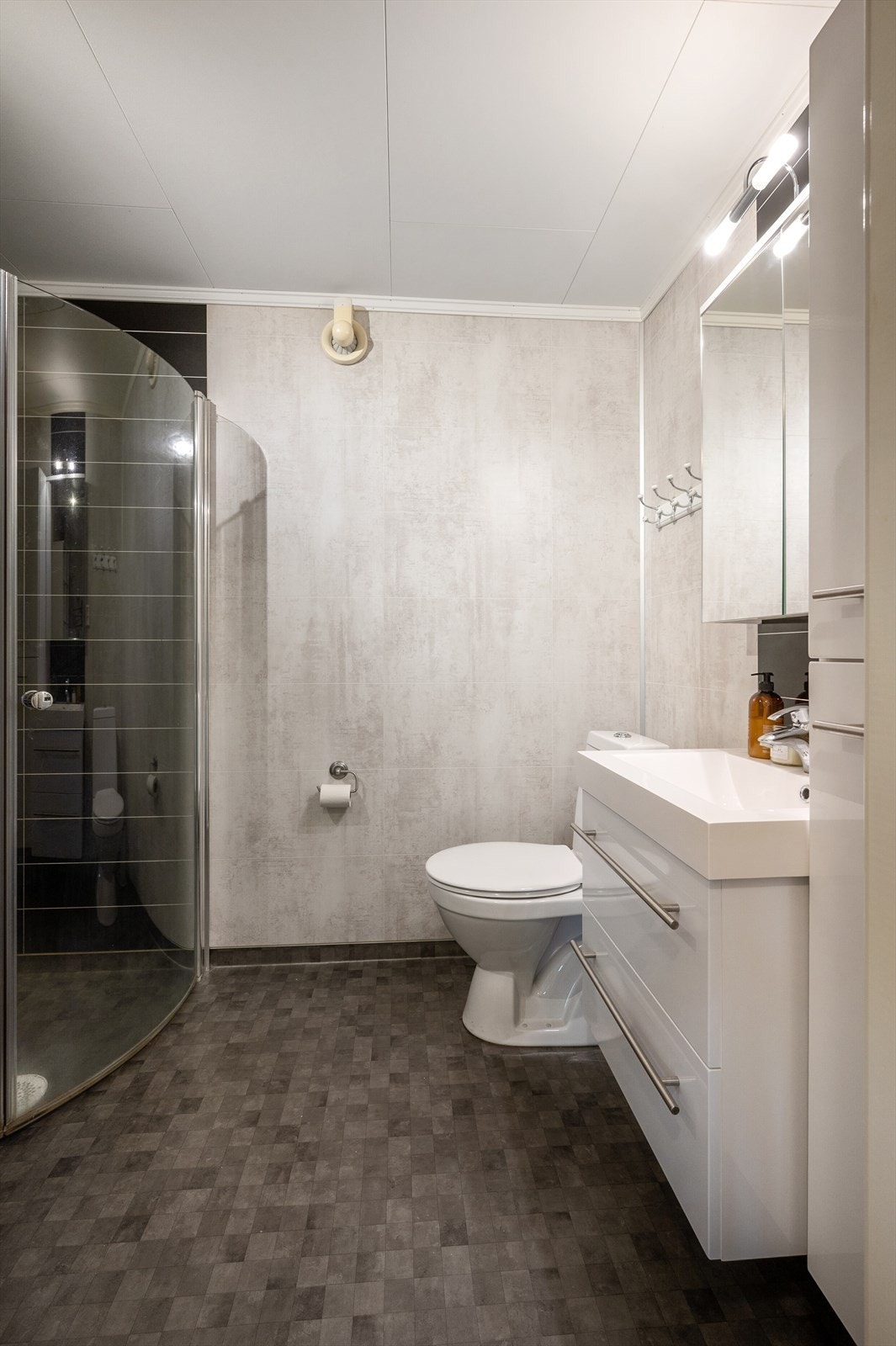 Nyere og tidløst bad fra 2015 bestående av gulvbelegg med oppbrett, våtromsplater på vegger og folierte plater i himling. Det er varmekabler i gulvet. Galleribilde