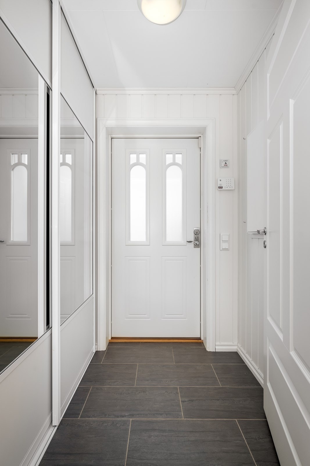 Lys og pen entré med flislagt gulv og praktisk skyvedørsgarderobe for skjult oppbevaring av sko- og yttertøy. Galleribilde