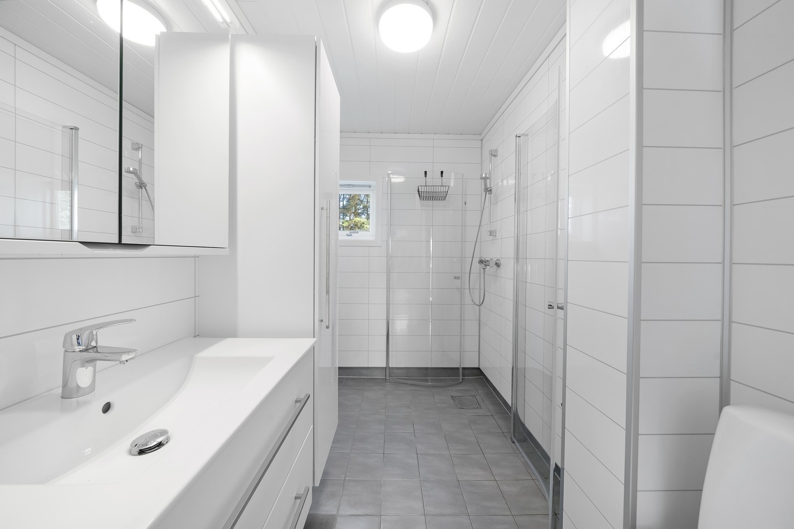 Pent bad med fliser med varmekabler på gulv og baderomsplater på vegg. Innredet med dusjnisje, toalett, baderomsinnredning og opplegg til vaskemaskin. Galleribilde