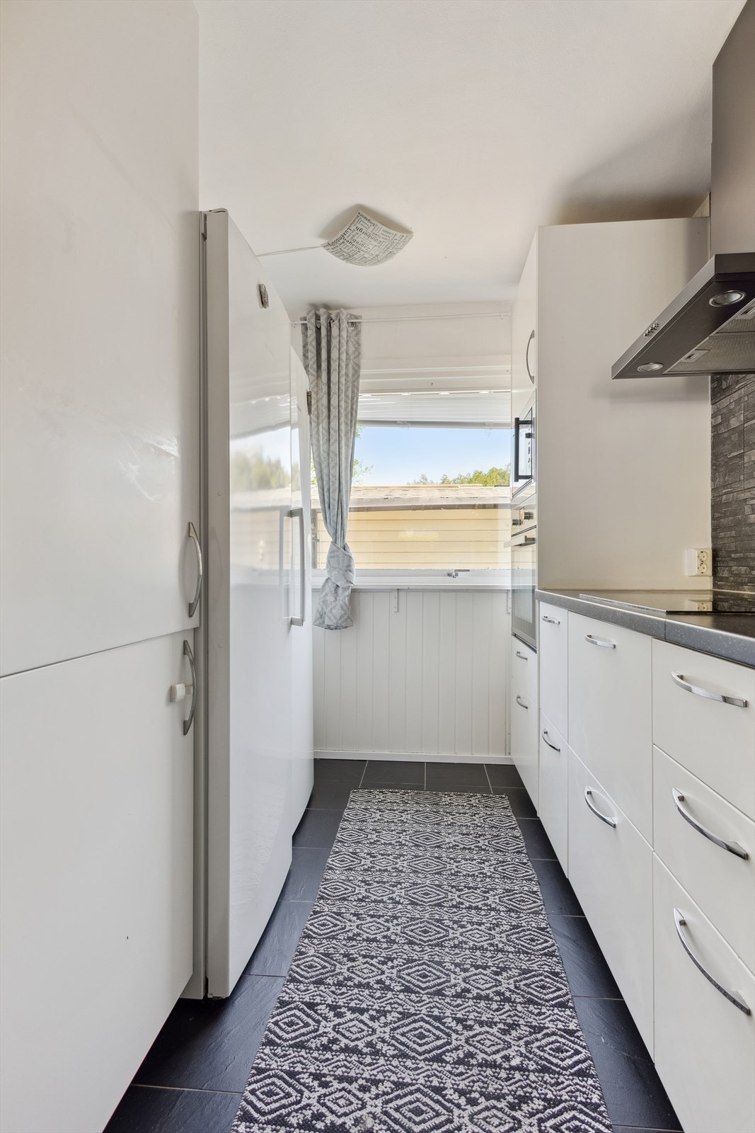 Ikea-innredningen har slette hvite fronter, vitrineskap og laminerte benkeplater. I innredningen er det integrert stekeovn og mikro i ståhøyde og platetopp, samt opplegg plass til oppvaskmaskin og frittstående kjøleskap. Galleribilde