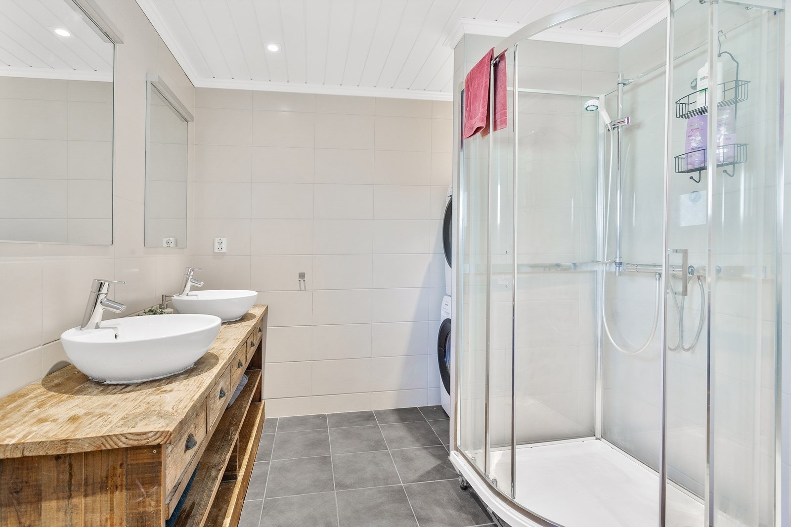 Badet er utstyrt med dusjkabinett, vegghengt wc og dobbel servantinnredning med kuleservanter, skuffer og hyller. Galleribilde