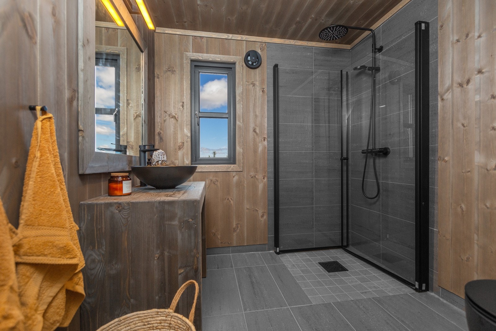 Hyttas tiltalende bad er innredet med mørke fliser på gulv og panel på vegg Galleribilde