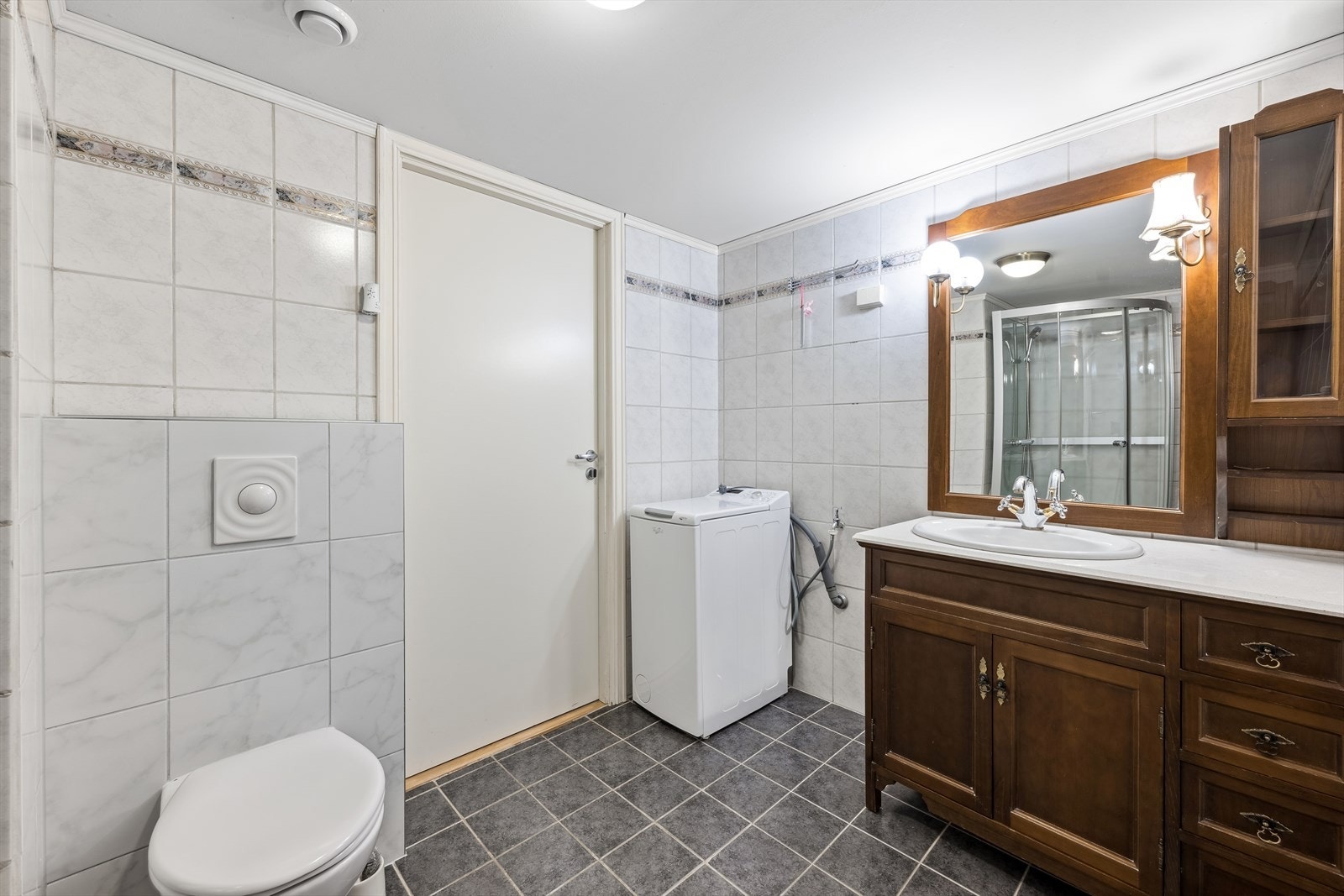 Pent flislagt bad med vegghengt wc, dusjkabinett, opplegg for vaskemaskin og innredning med vask. Galleribilde