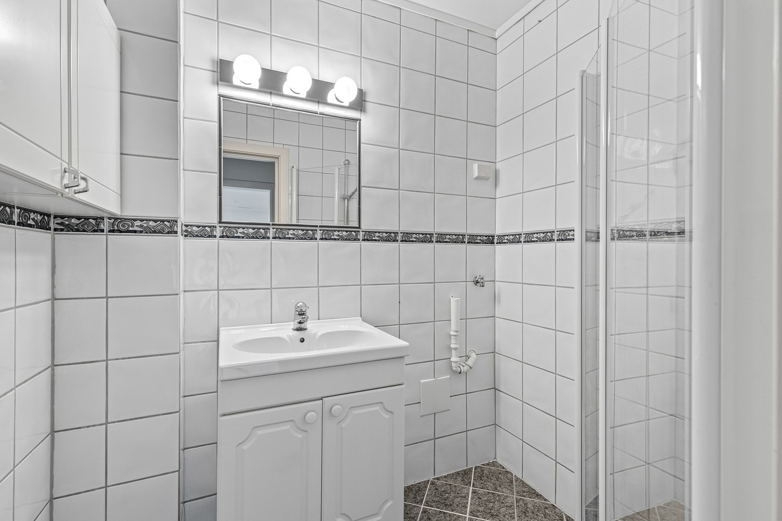 Lyst, flislagt bad innredet med servant og dusj med innfellbare dører. Galleribilde