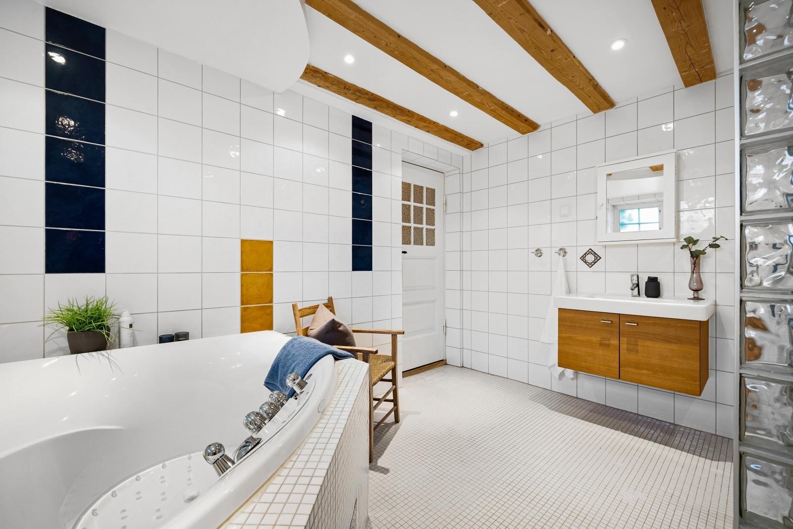 Badet inneholder dusj med innfellbare dører i herdet glass, badekar, servant i helstøpt plate og klosett samt veggskap med speil. Galleribilde