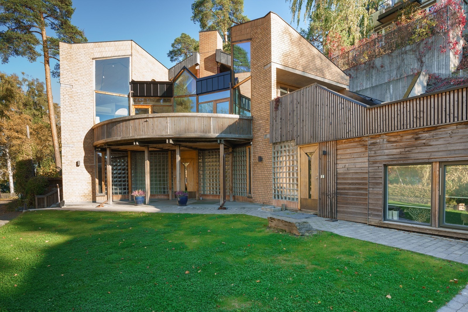 Tomt for boligen opparbeidet med plenarealer, busker, diverse beplantning, belegningsstein og naturtomt. Påbygget til høre i bildet er søkt revet. Galleribilde