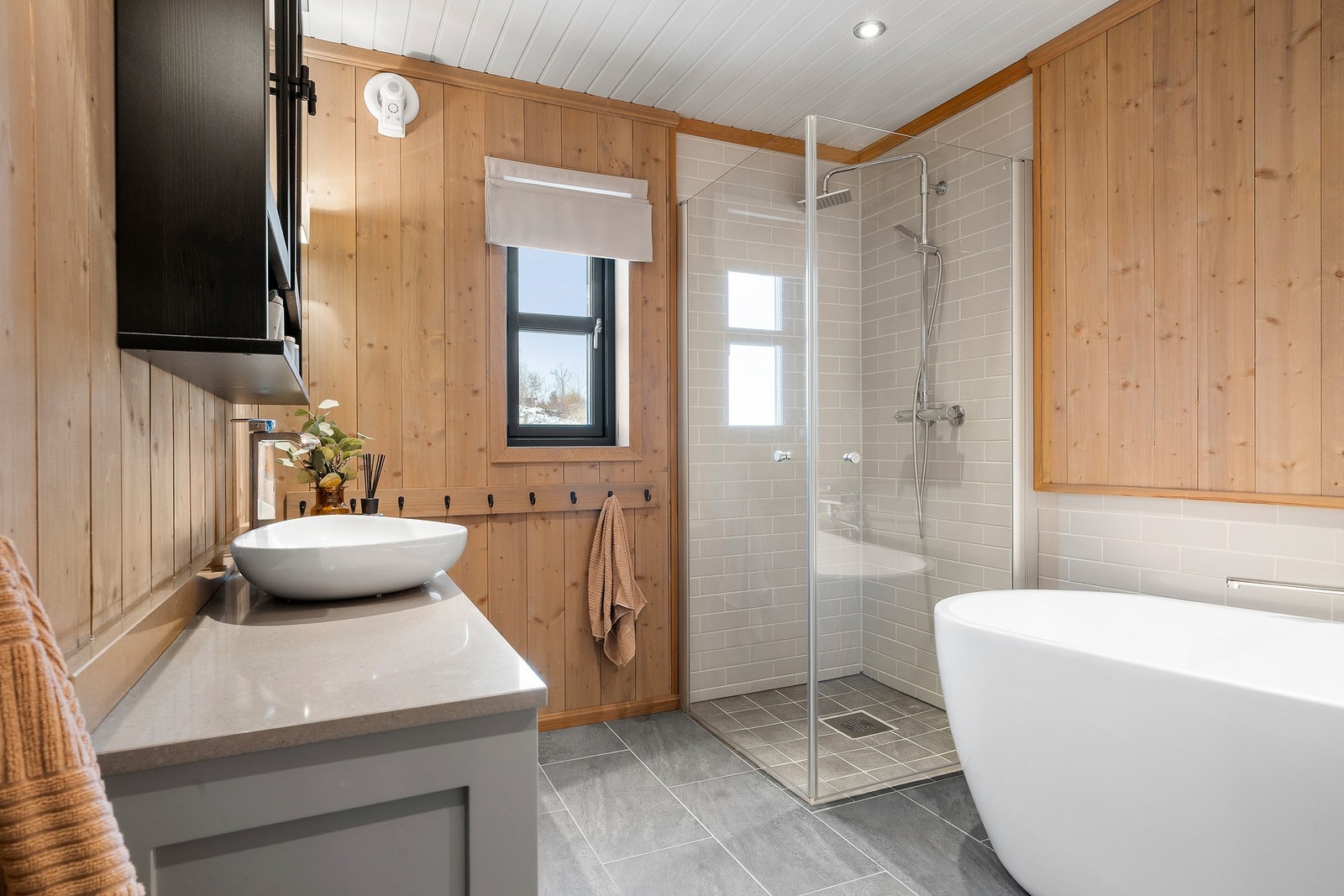 Badet har flotte gulvfliser med gulvvarme, flislagt dusjsone, panel på vegger, og panelt tak med downlights. Galleribilde