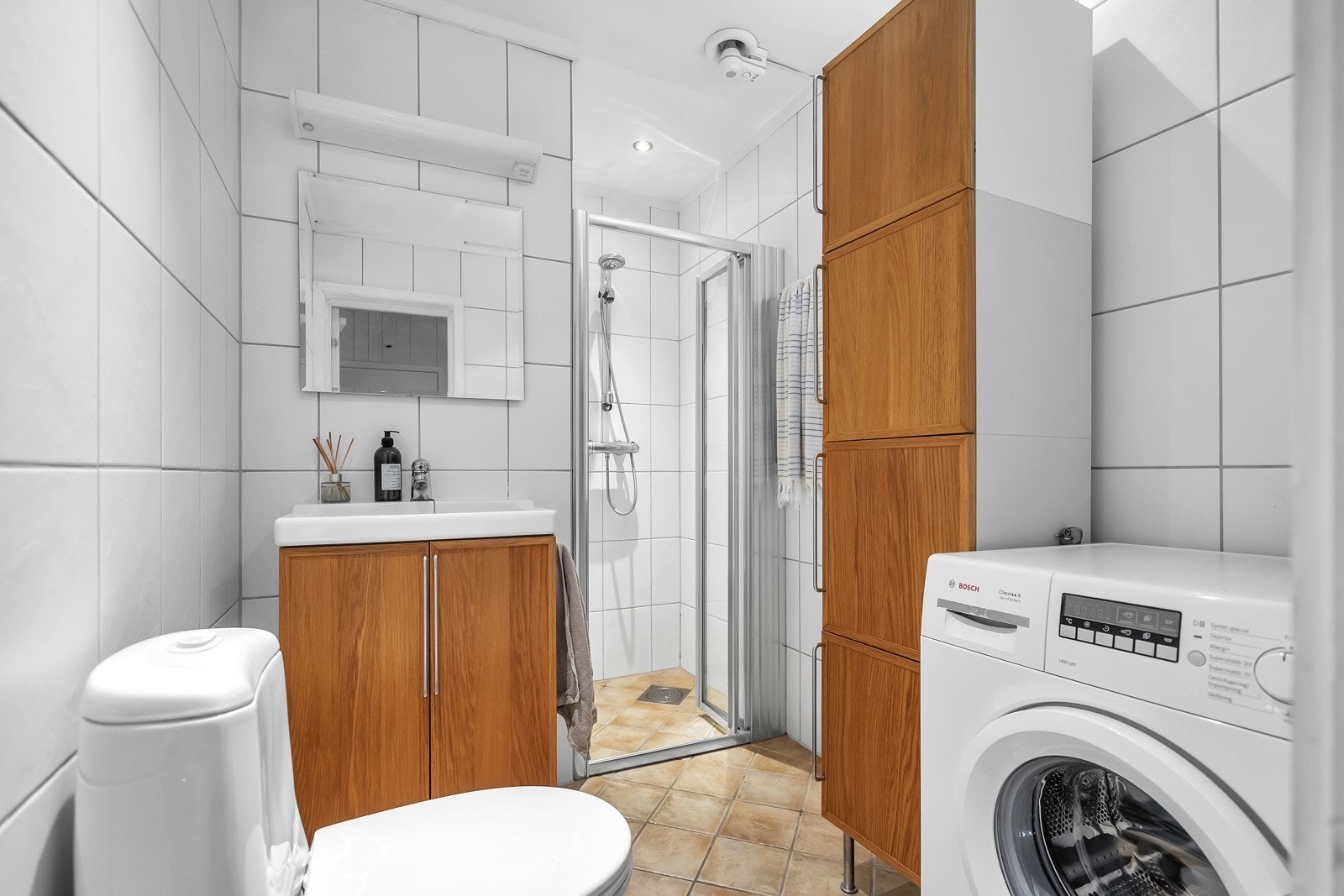 Flislagt bad med toalett, servant med innredning, dusjnisje og opplegg til vaskemaskin Galleribilde