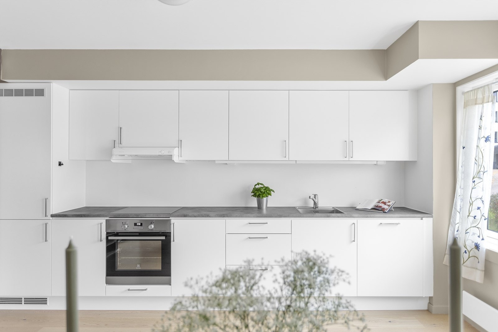 Hvit, glatt innredning med skuffer og skap, samt grå benkeplate av laminat. Integrerte hvitevarer som stekeovn, platetopp, oppvaskmaskin, samt kjøle/fryseskap medfølger. Galleribilde