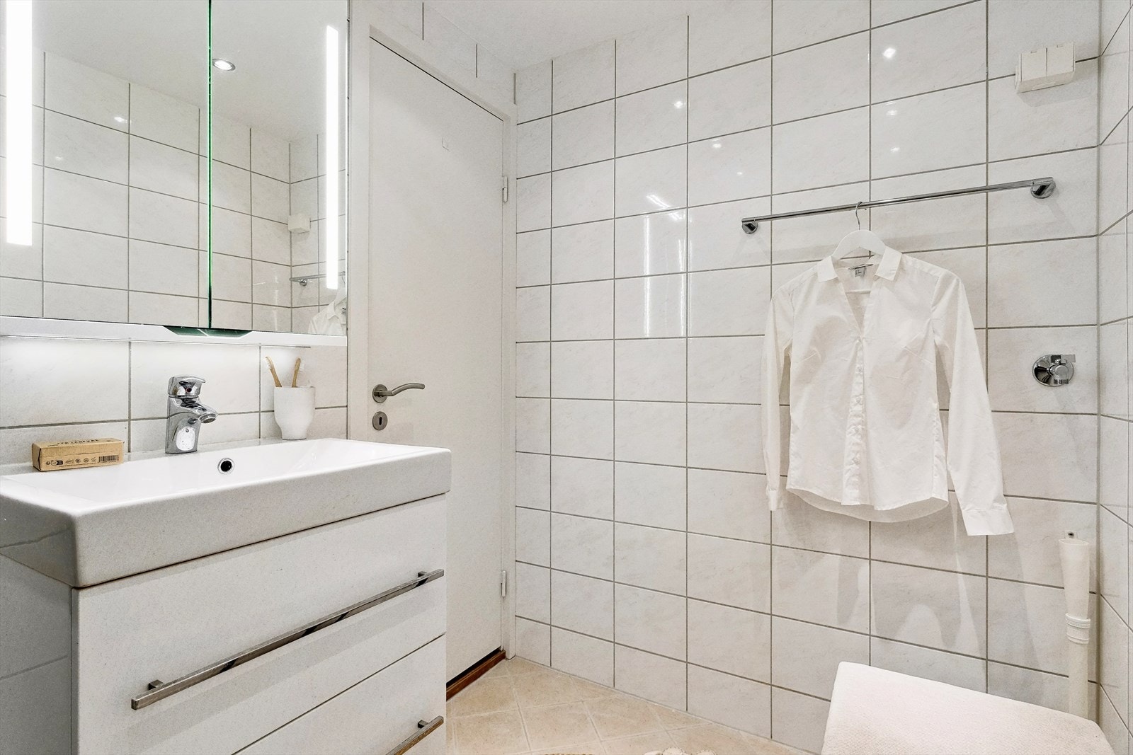 Baderommet har dusj direkte på gulv med innfellbare dører og servant med tilhørende skuffeseksjon. Speilskap med belysning over servant. Galleribilde