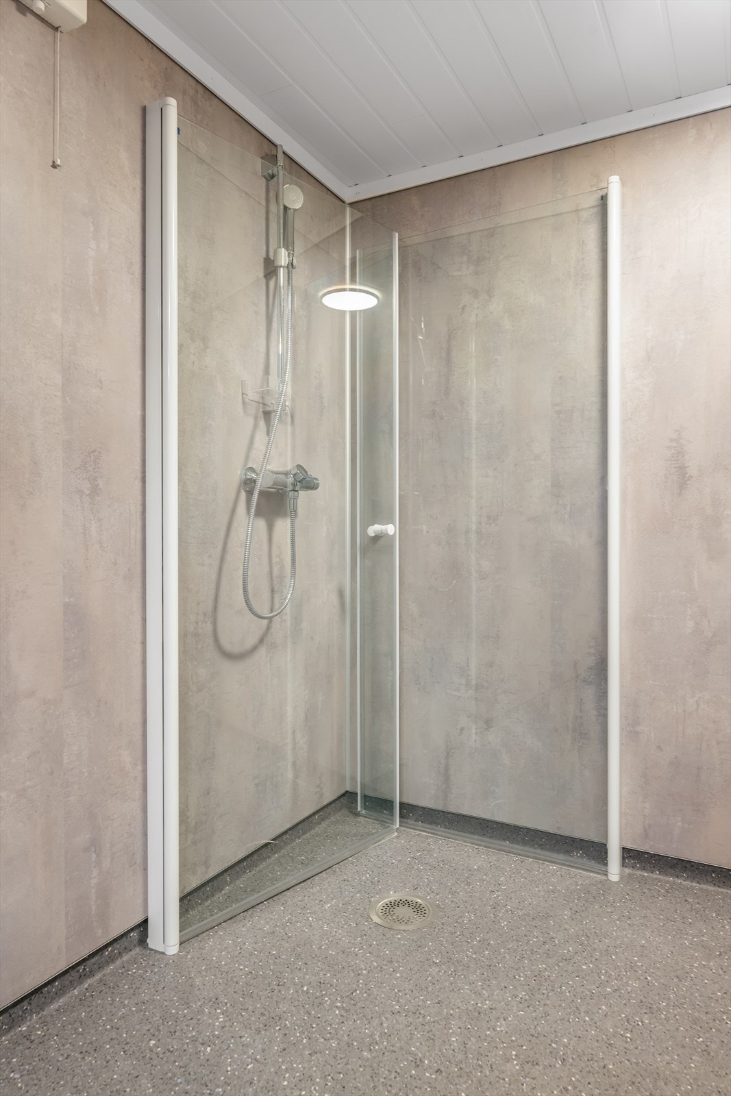 Dusjnisjen har dusjdører som kan felles inn. Overflater består av belegg på gulv og våtromsplater på vegger, samt MDF-panel i tak. Galleribilde